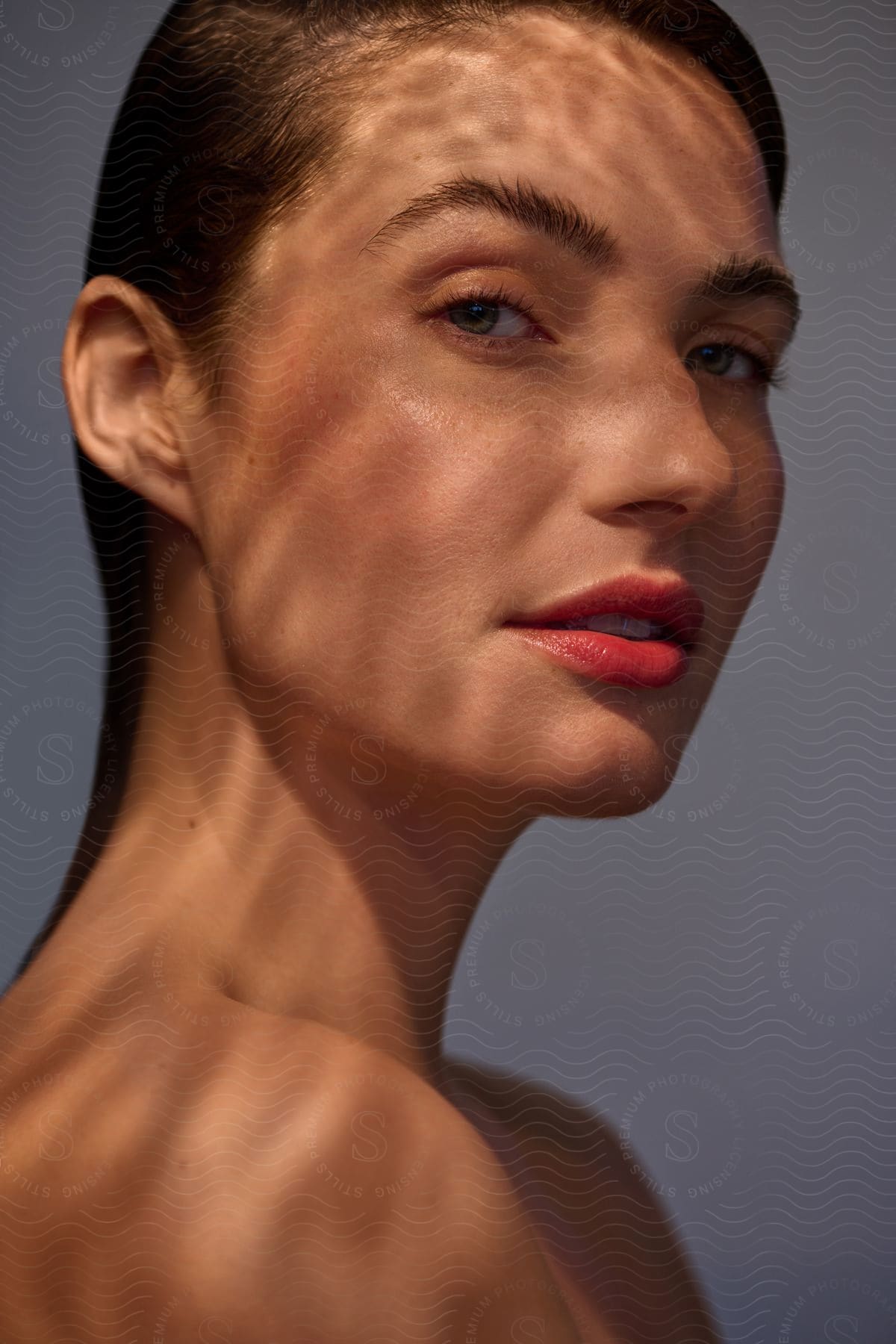 Light shines on the face of a woman wearing red lipstick as she looks from her side