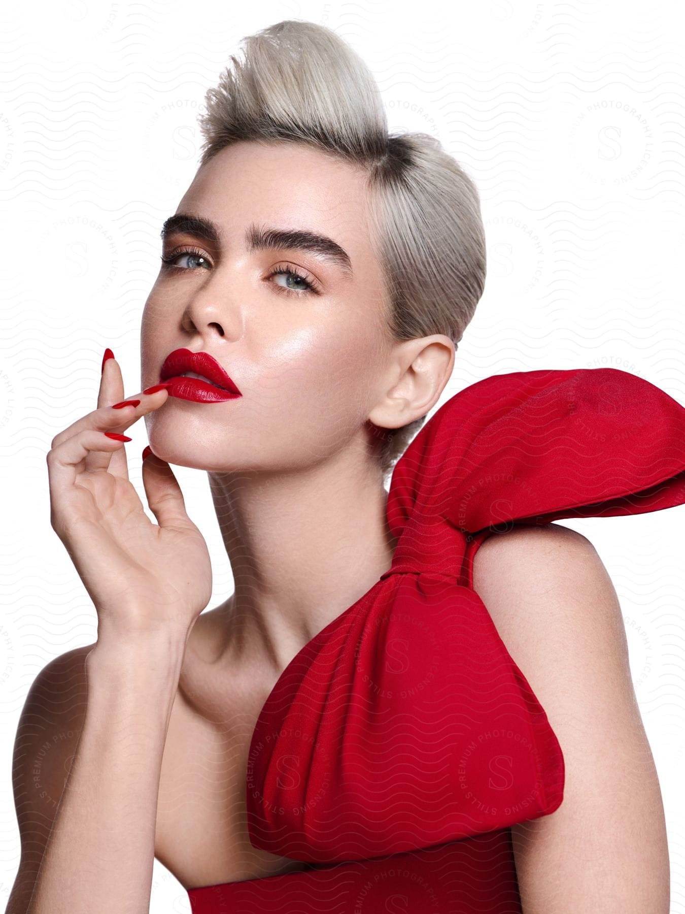 Woman wearing lipstick and red dress with red bow on shoulder touches her lips with hand