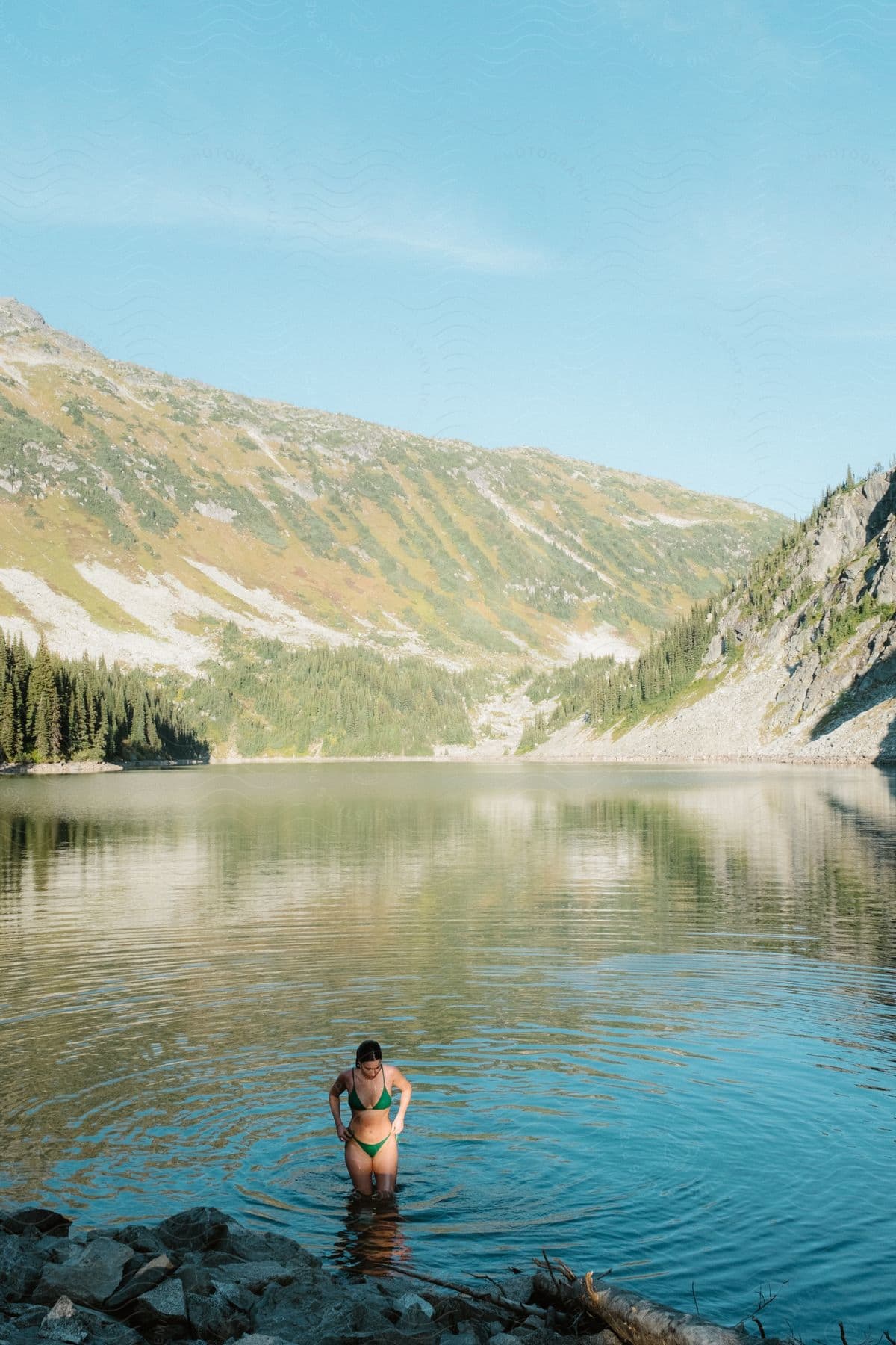 Stock photo of a woman in a bikini coming out of a lake surrounded by mountains.