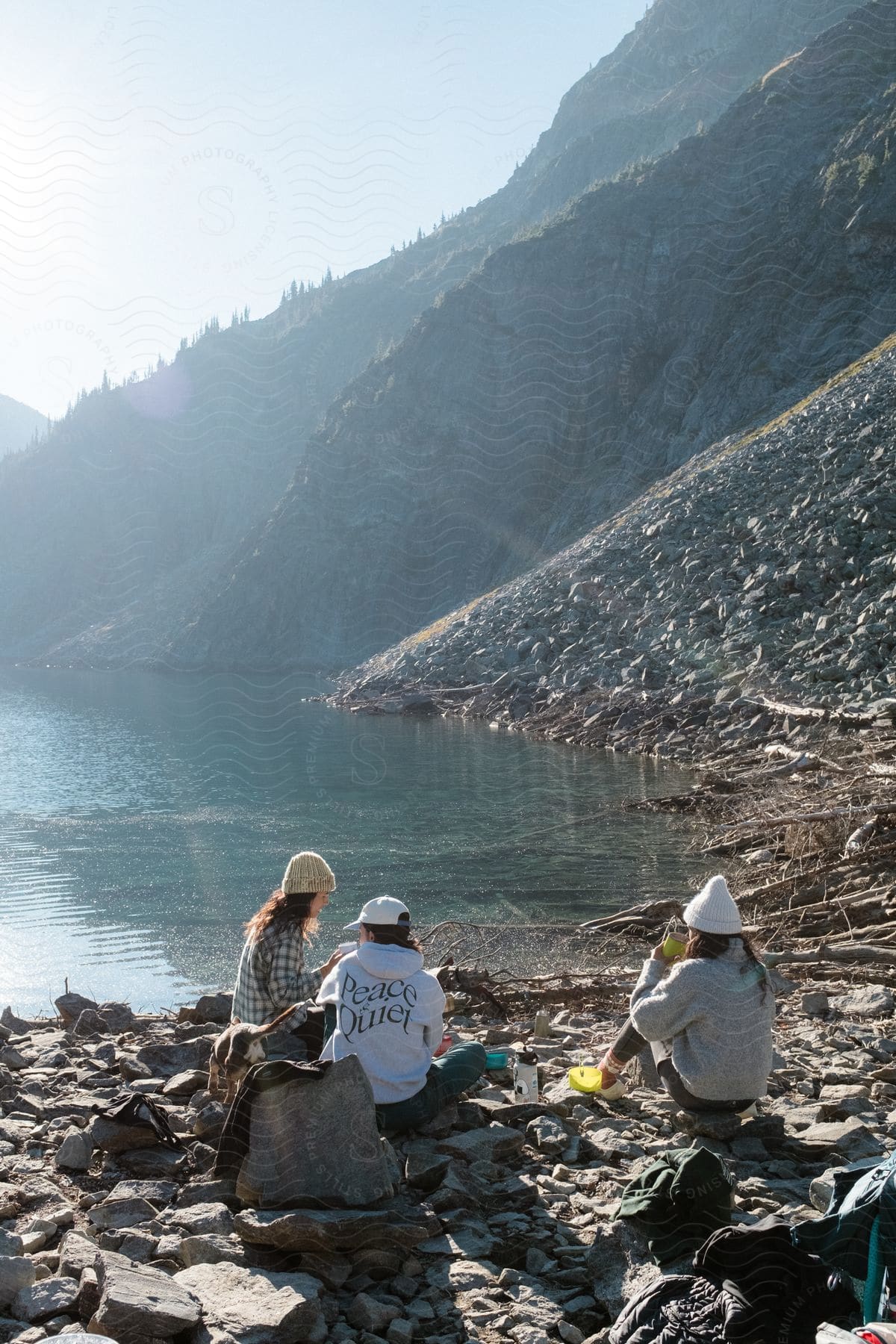 Three women in autumnal attire rest on rocks by a lake, bathed in the golden glow of the sun.