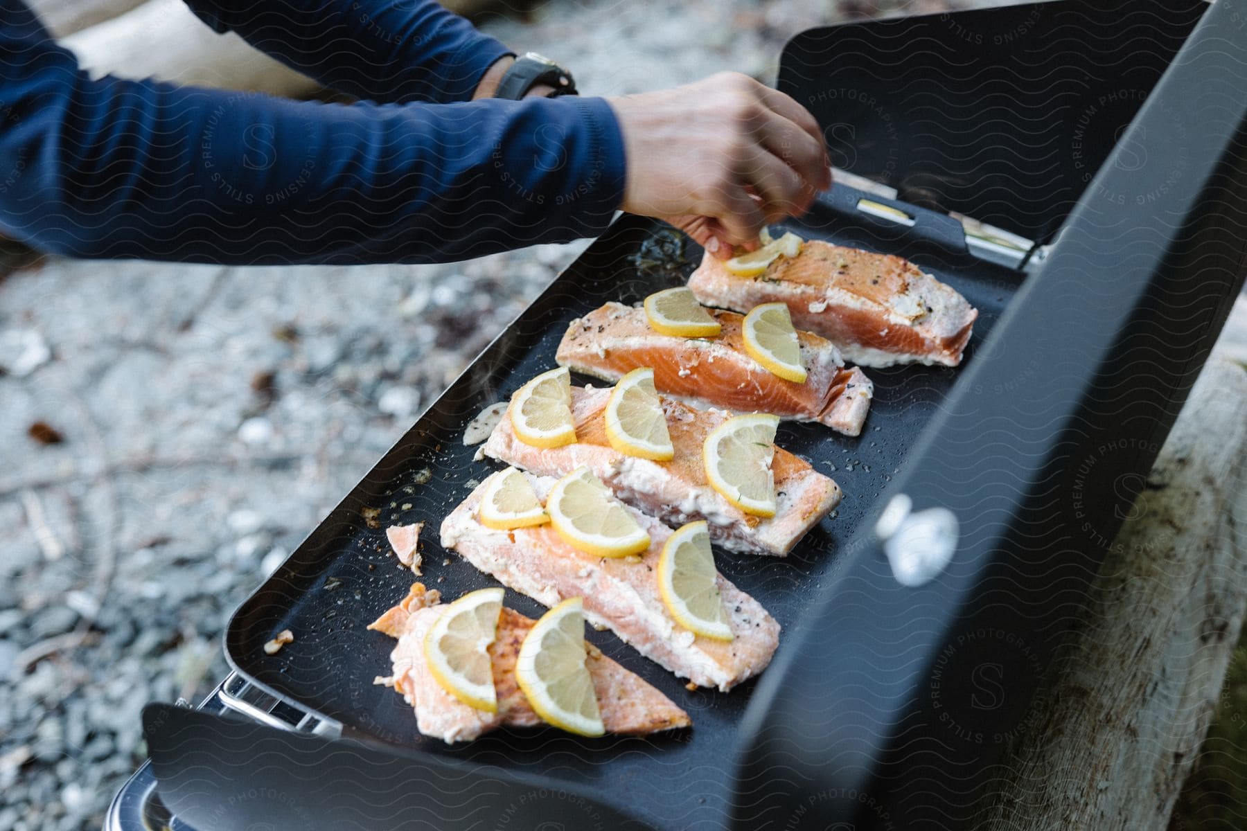 Woman cooks fish on grill set on outdoor ledge.