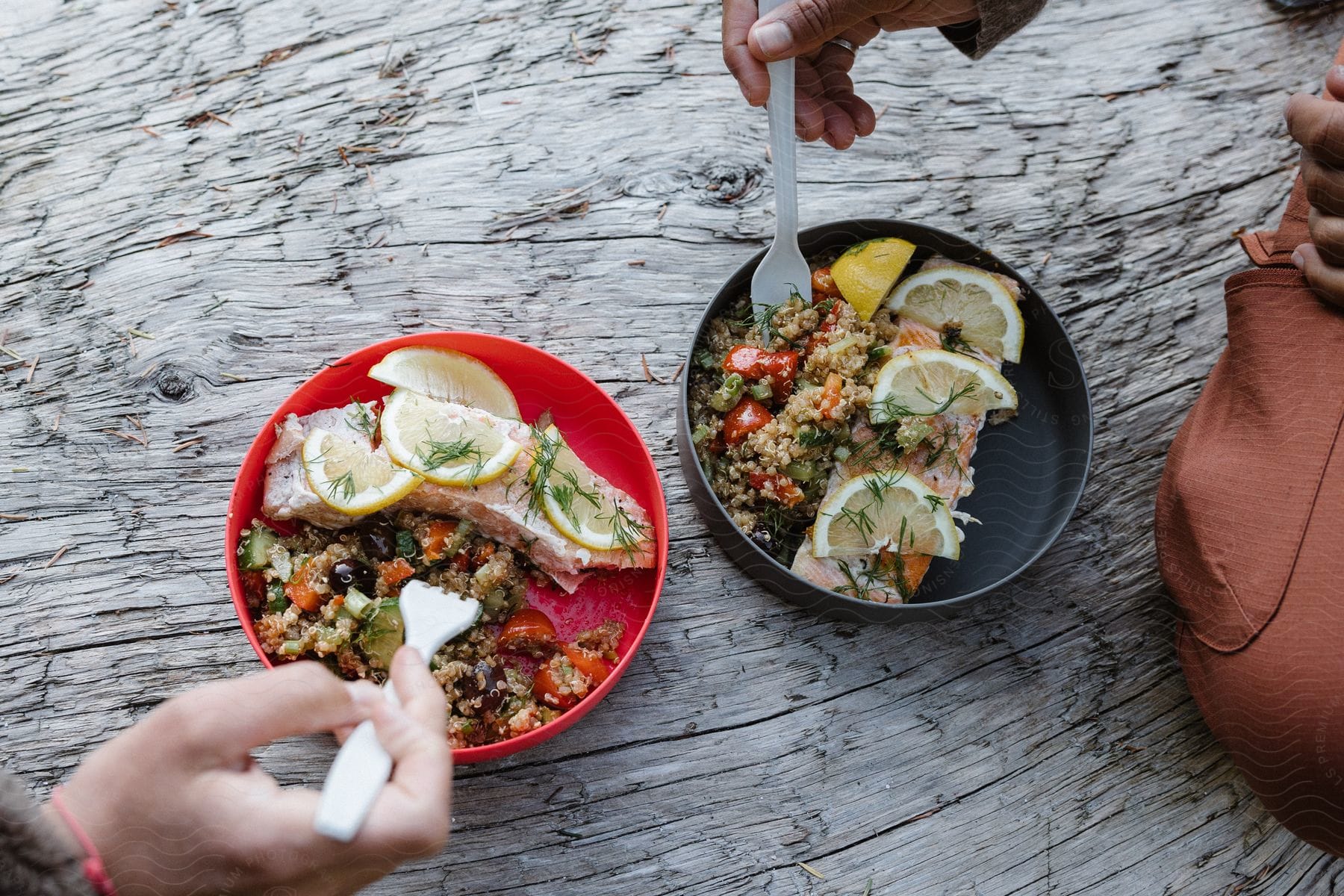 Two plates with fish protein, quinoa, and two hands with forks in the bowls of the plates.