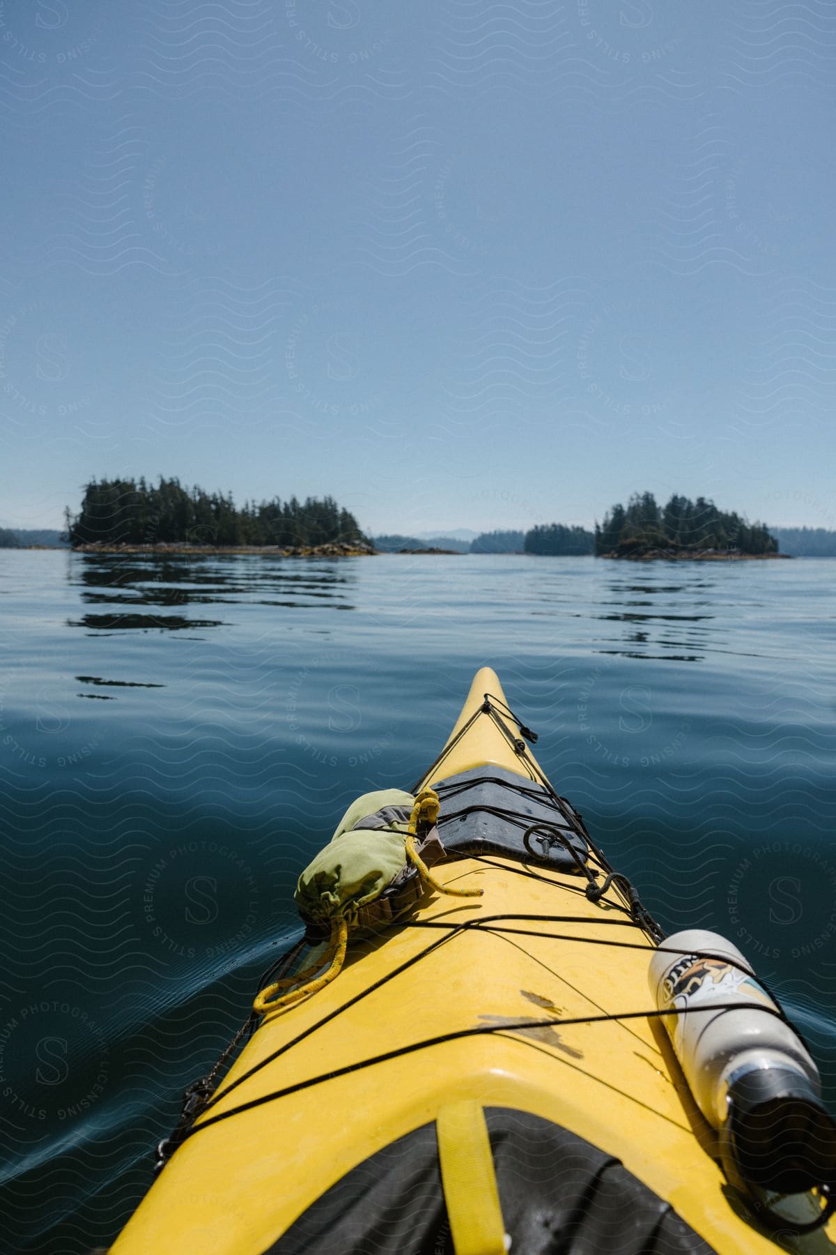 A bright yellow kayak floats on crystal-clear waters, with a lush green island in the distance and a cloudless blue sky overhead.