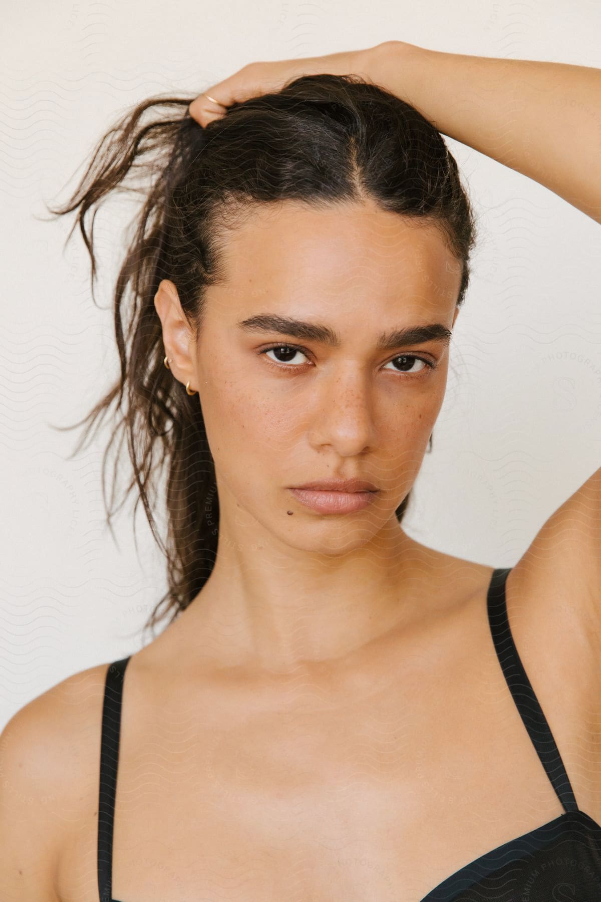 A model is pulling her dark hair back with her hand as she stares deeply at the camera.