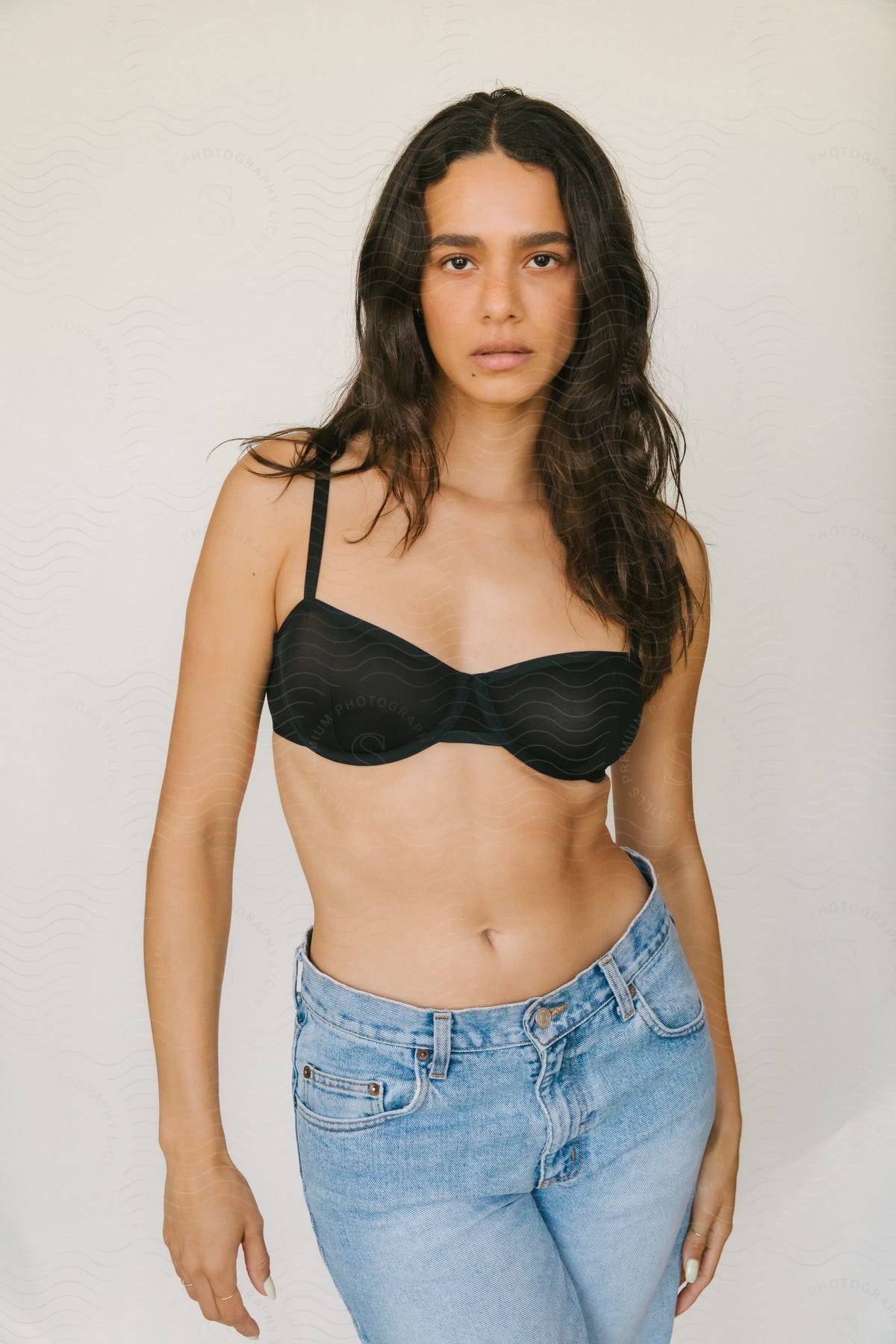 A young woman poses in jeans and a black bikini top.