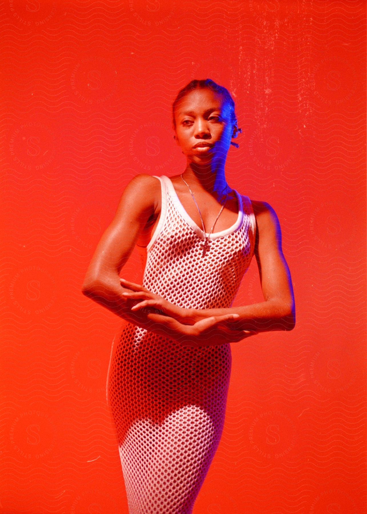 Woman posing against a red background in a long white dress.