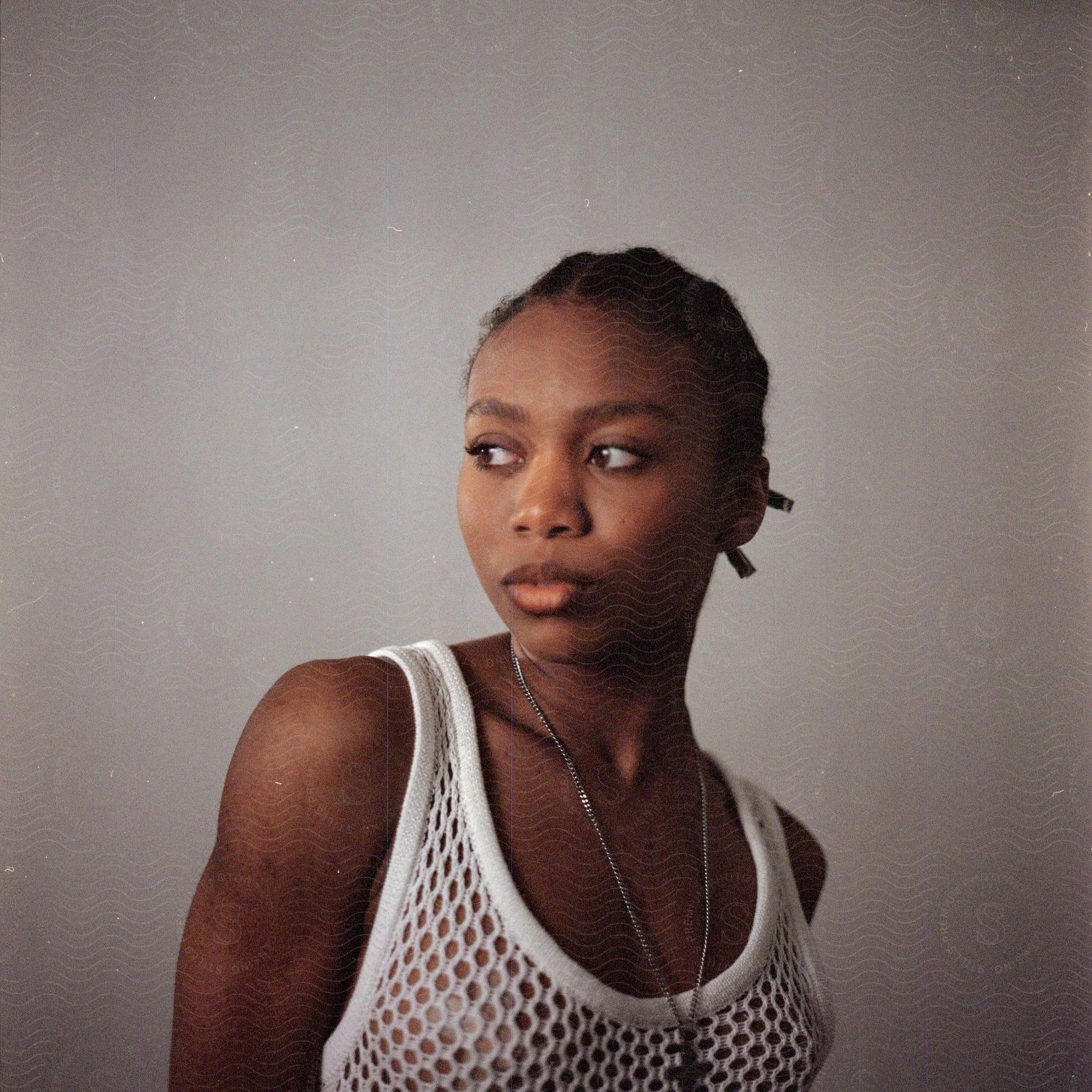 An African American woman with a chain necklace and white wife beater poses for a picture on a white background.