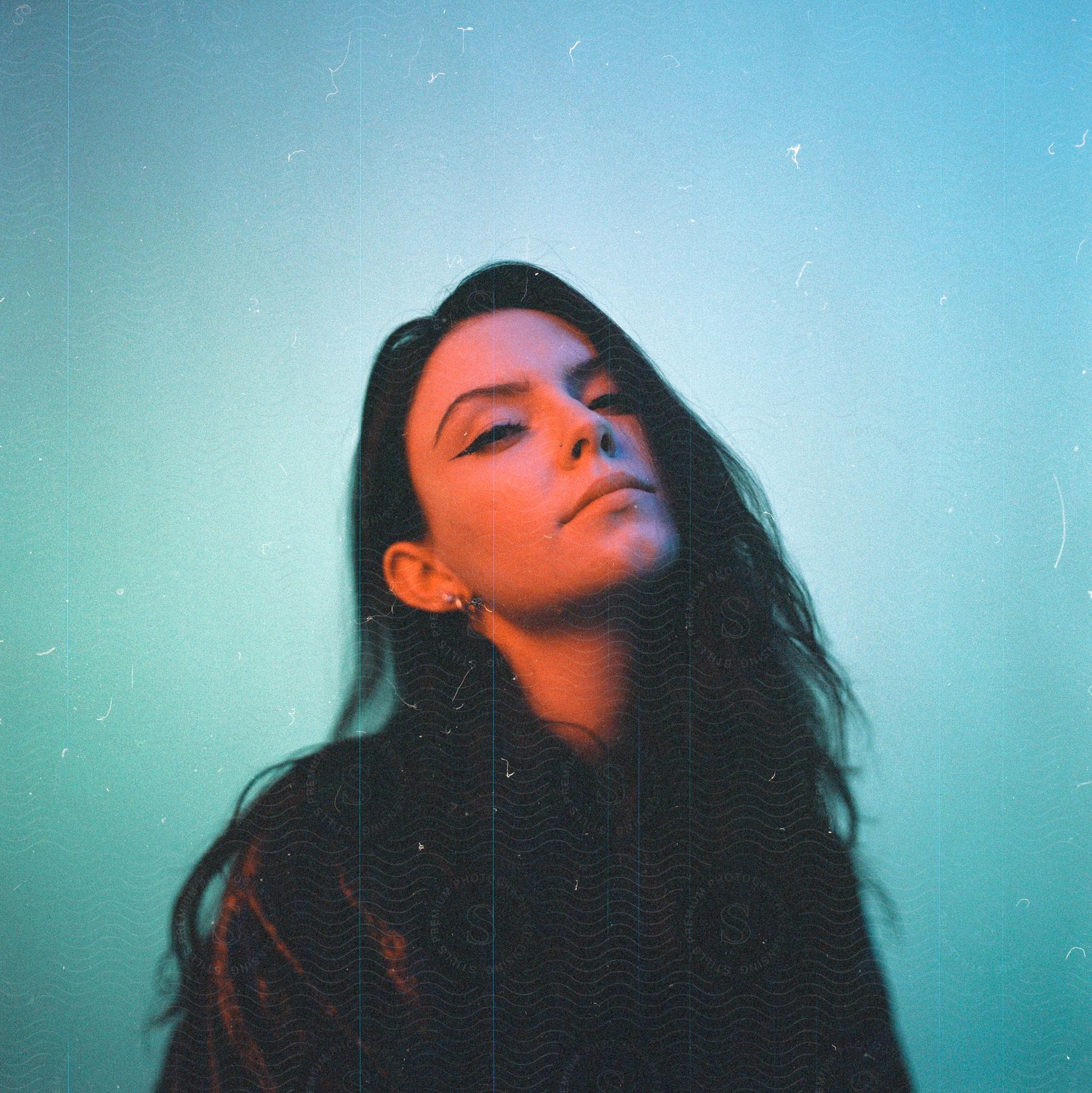 A woman with long black hair is posing with her head tilted to the side