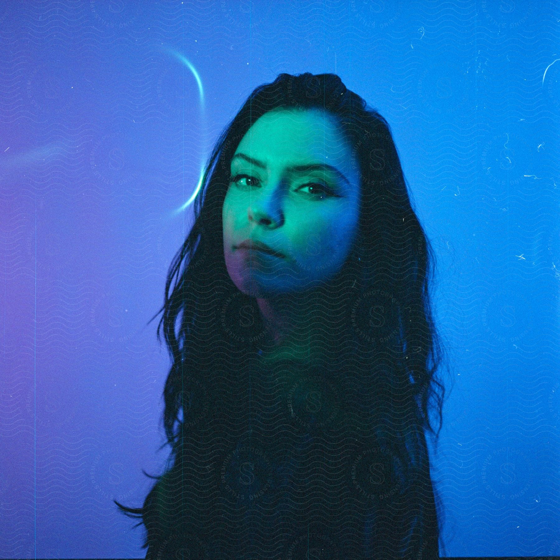 A woman with long hair stands in front of a blue background, bathed in blue light.