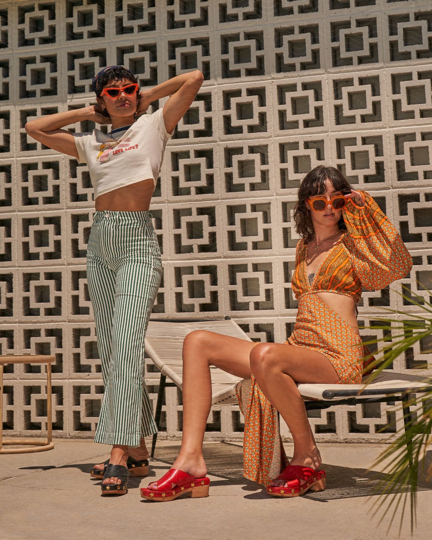 Two women are modeling summer fashion on a patio during the day.