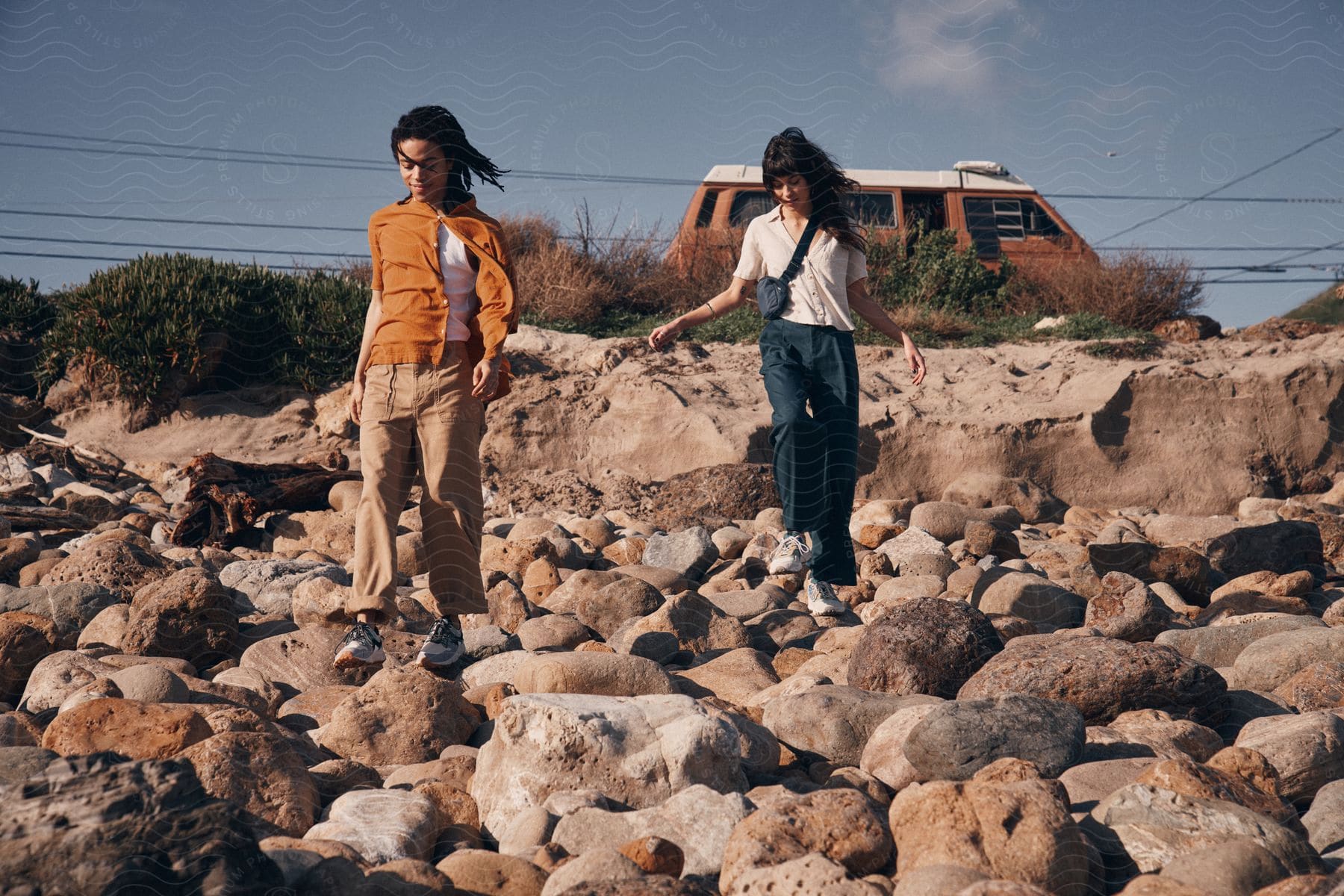 Two young women are walking on rocks down a hill and their van is parked on the road in the distance