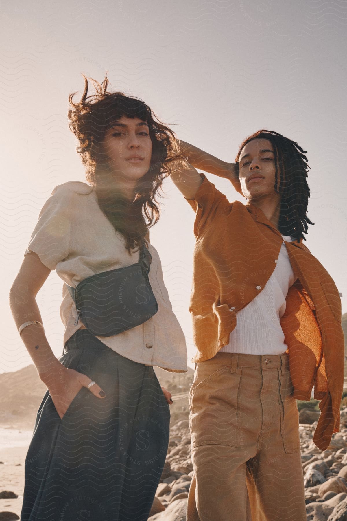 Male and female fashion models pose on beach on windy day.