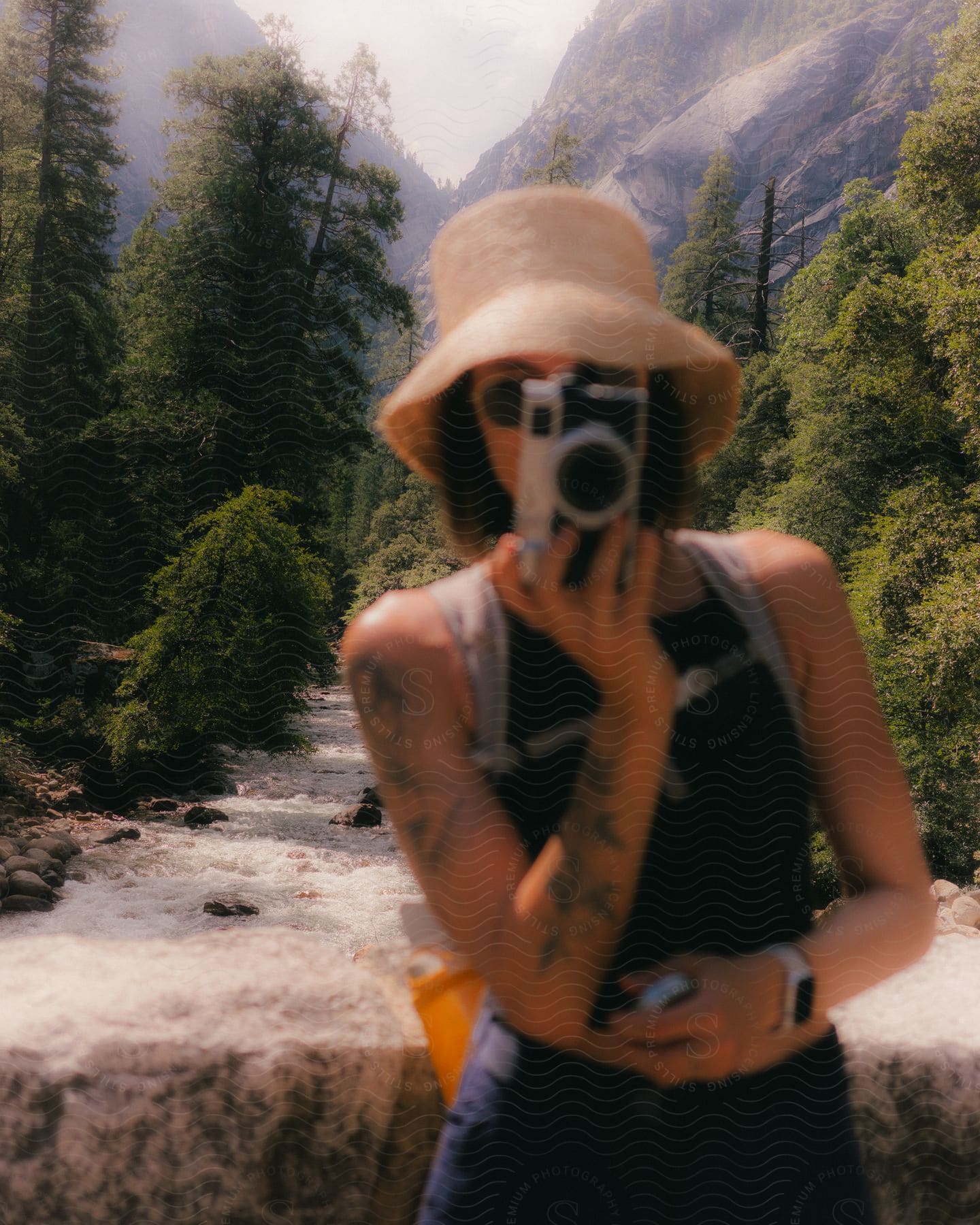 a woman holds up a camera while standing in front of a river in a canyon