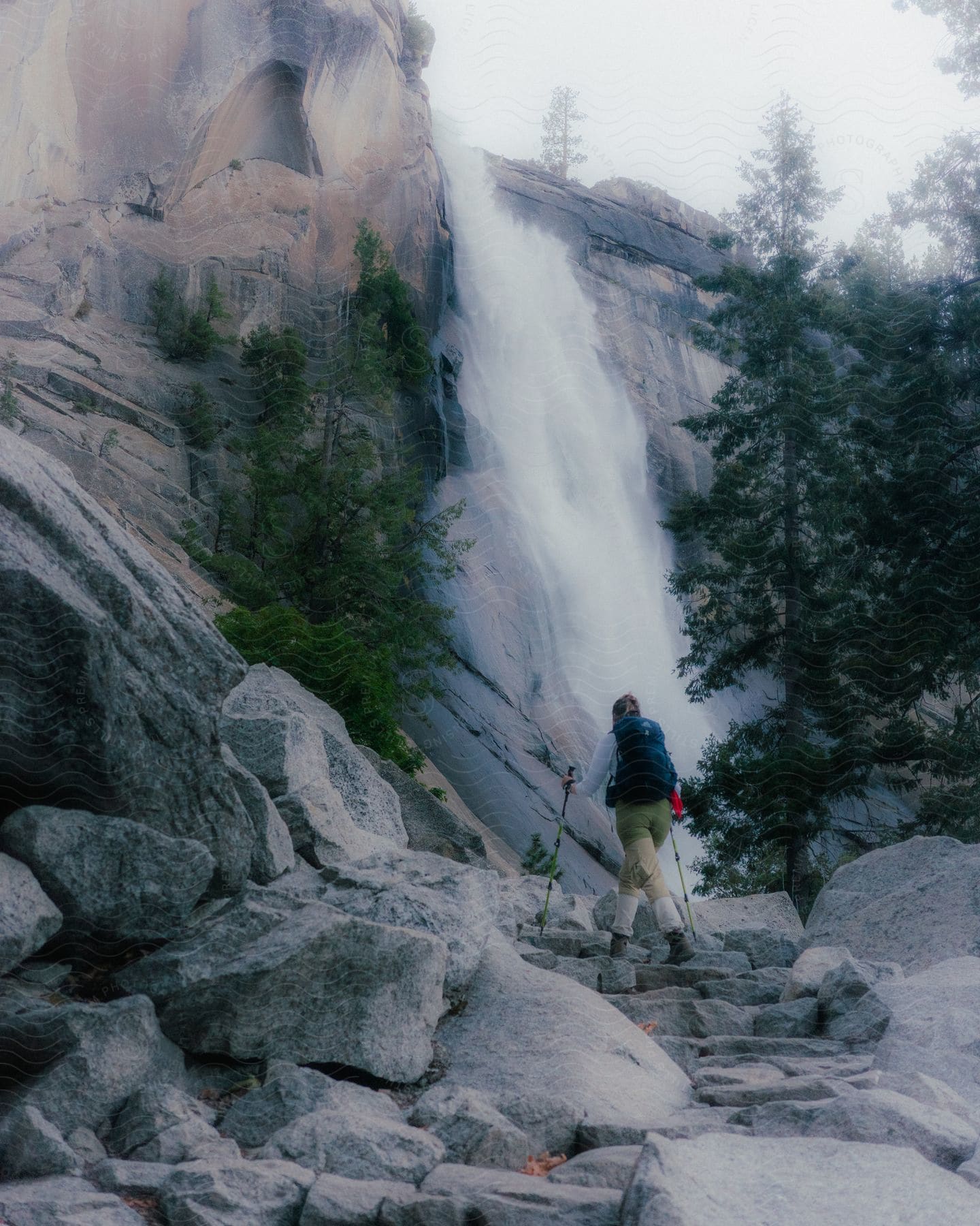 A woman with accessories hiking in a natural environment with rocks and a waterfall.