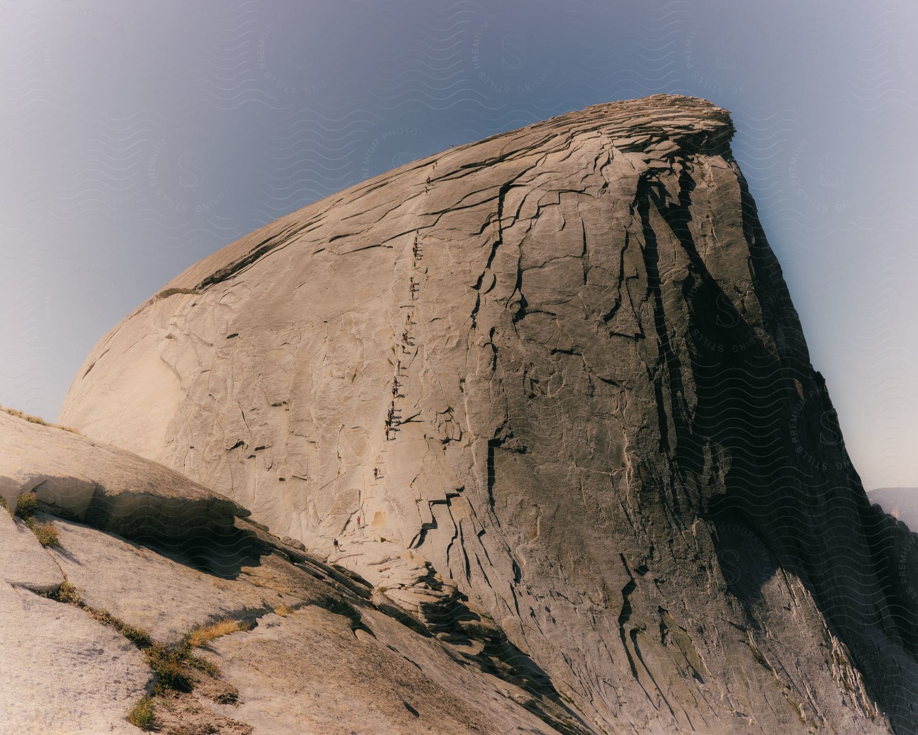 Under a partly cloudy sky, a large mountain hill rises with a small patch of grass growing in its rocky base.