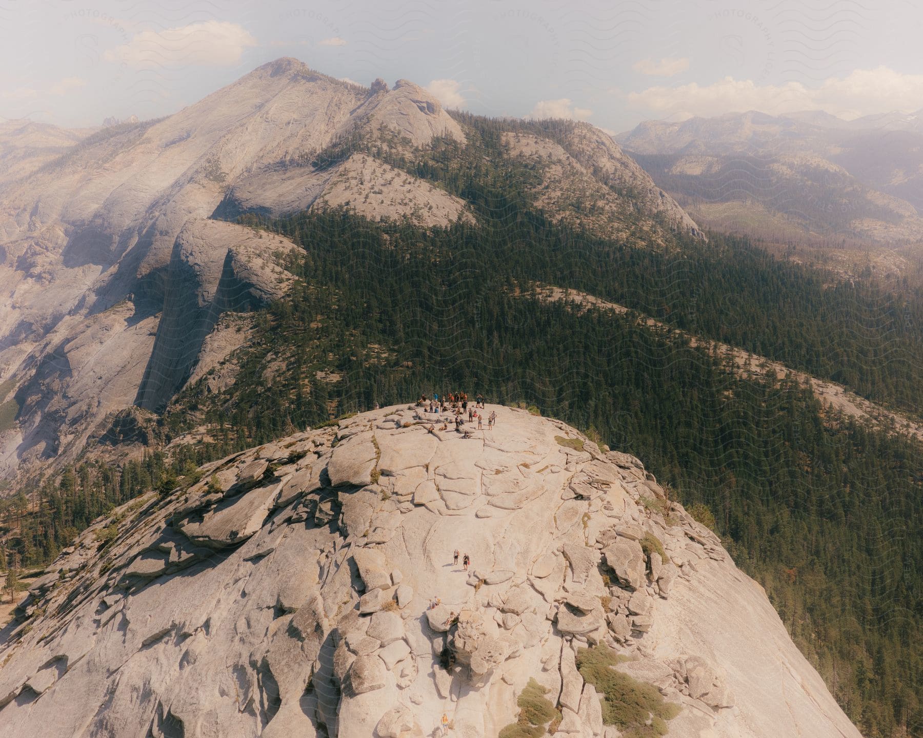 People standing on a mountaintop, overlooking a forest and a forest-covered mountain range.