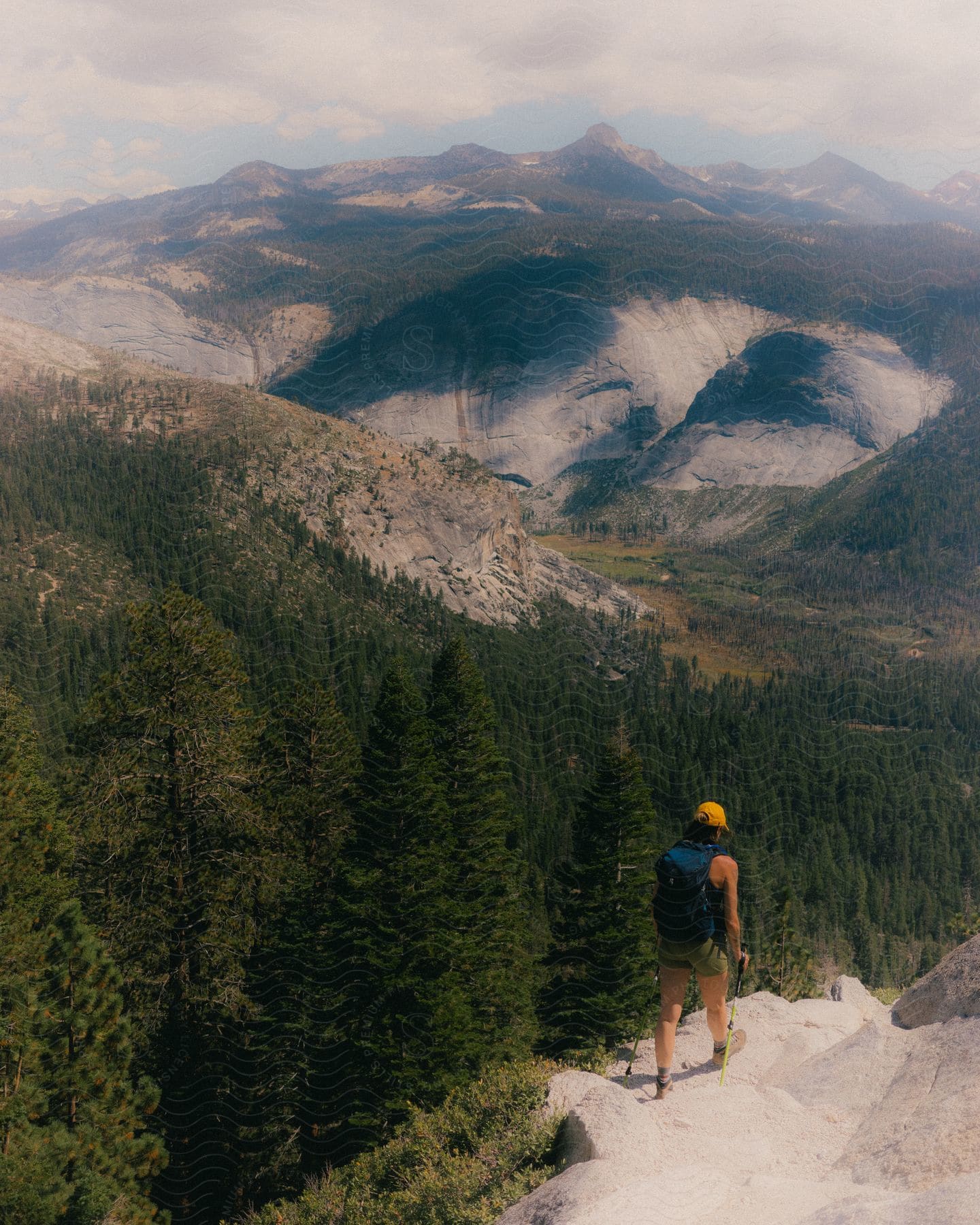 Overlooking the mountains, a backpacker hikes down passing the trees.