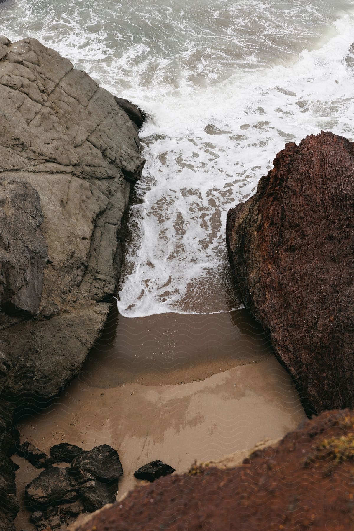 Looking down a cliff wall with large rocks and sand in a coastal region on an overcast day.