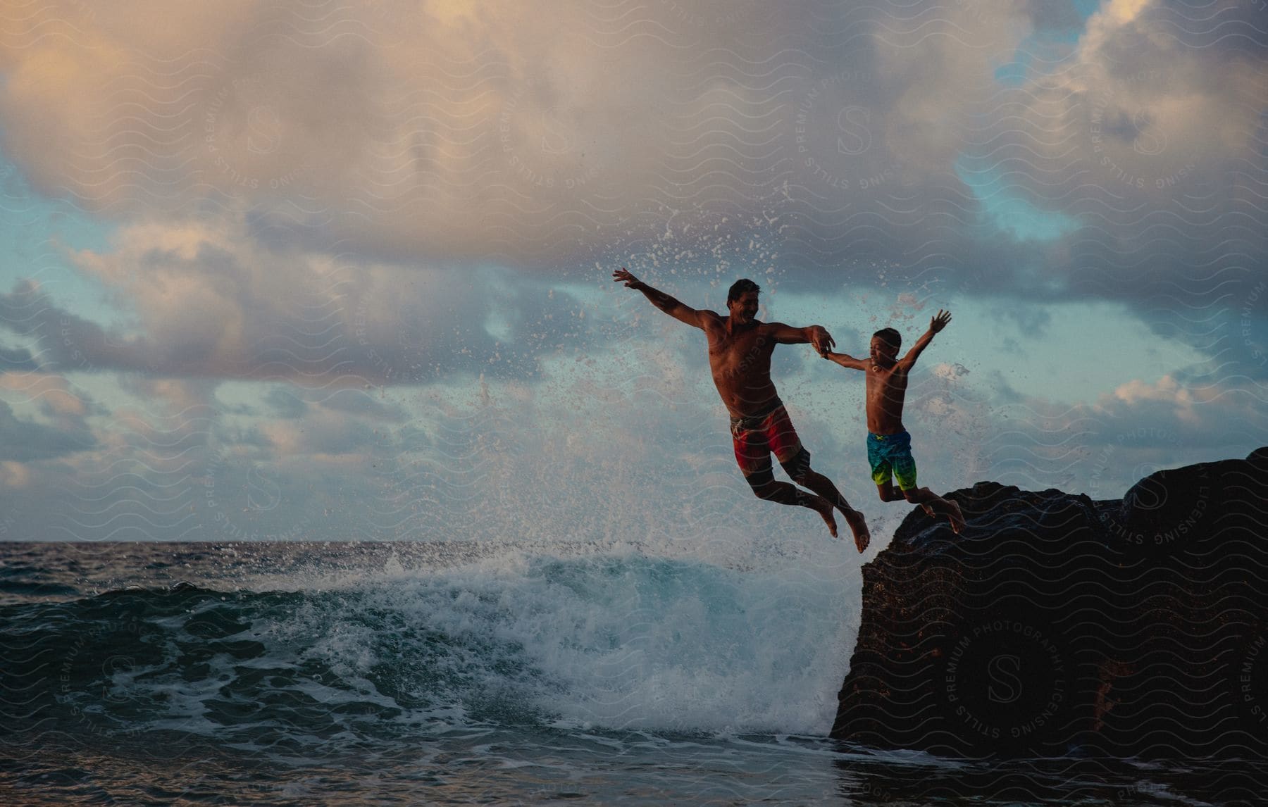 A father and son are jumping from the rock into the water.