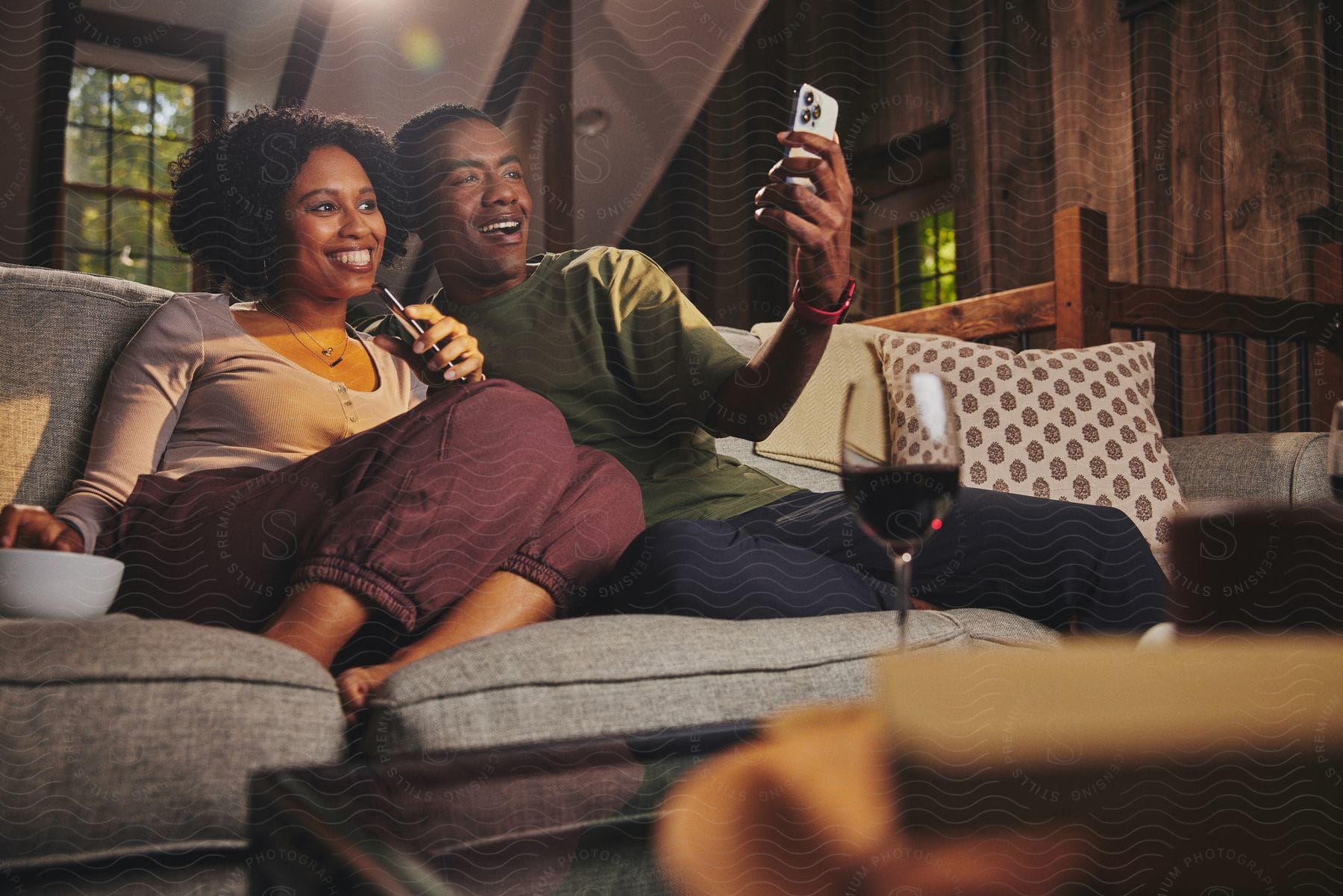 A man and a woman sitting on the sofa looking at their cell phones and smiling.