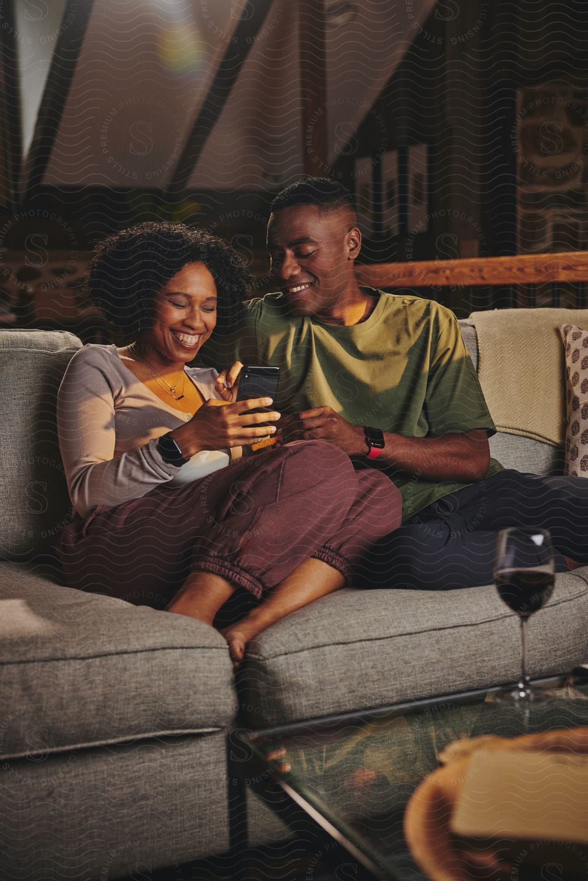 A couple of friends sitting on the couch while looking at the cellphone held by the woman.