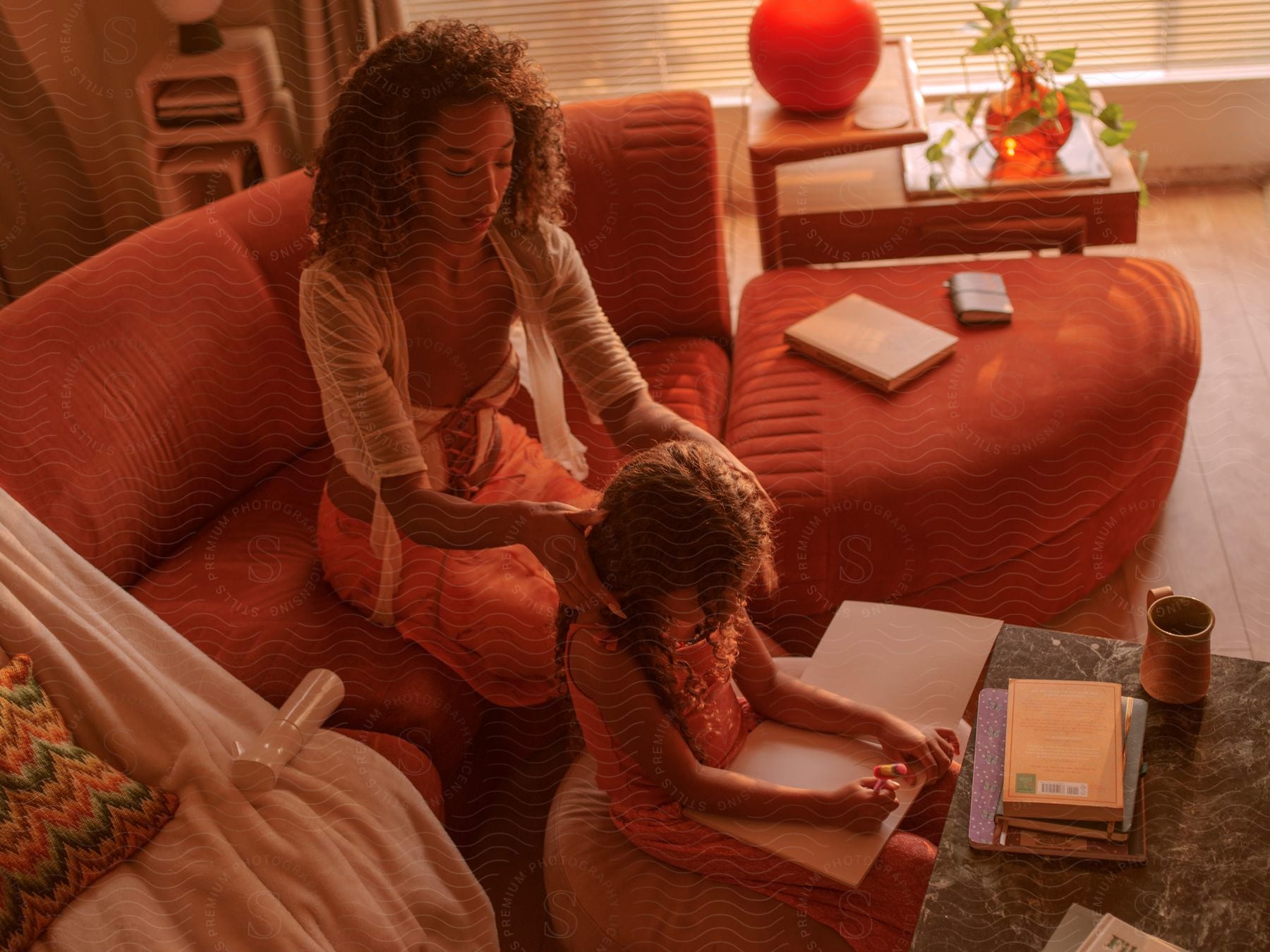 As the mother does her daughter's hair, the daughter makes a drawing in a notebook