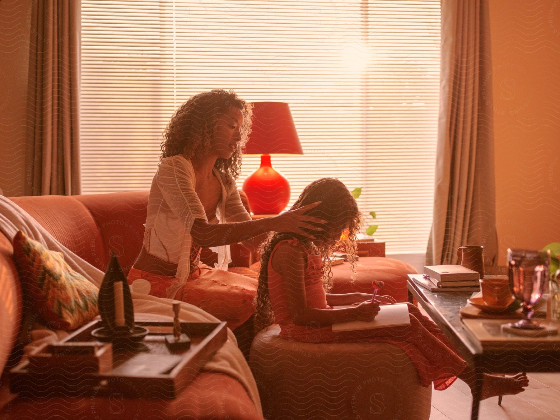 A daughter draws while her mother does her hair in a living room.