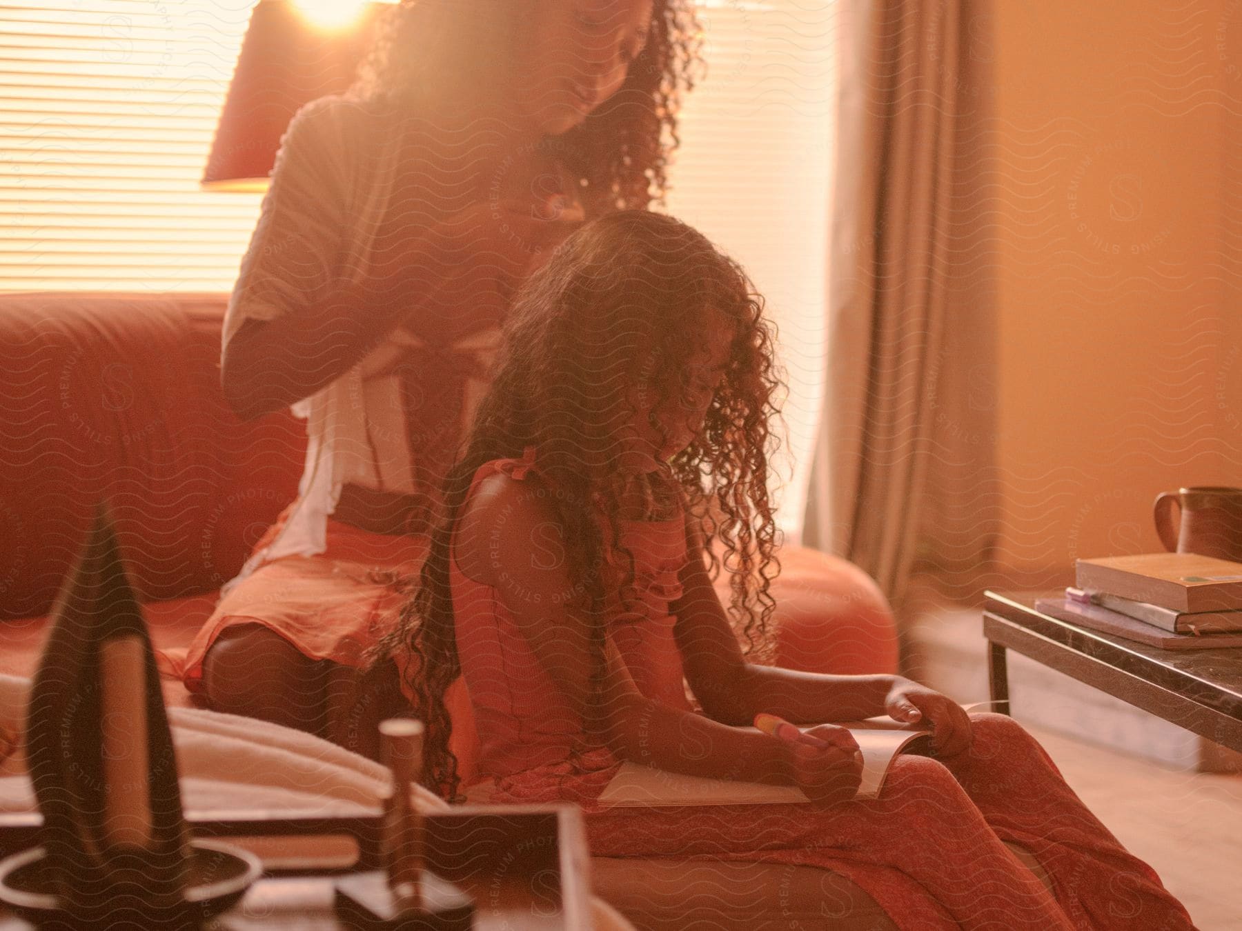 A mother combing her daughter's hair while she draws.