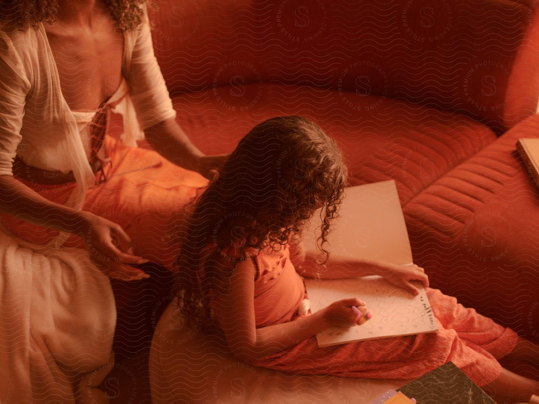 A mother fixing her daughter's curly hair while she draws.