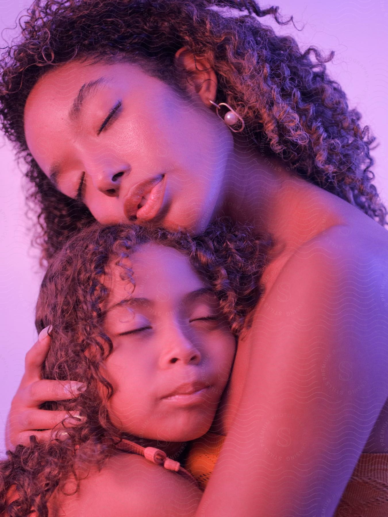 A mother and daughter with light curly hair hugging.