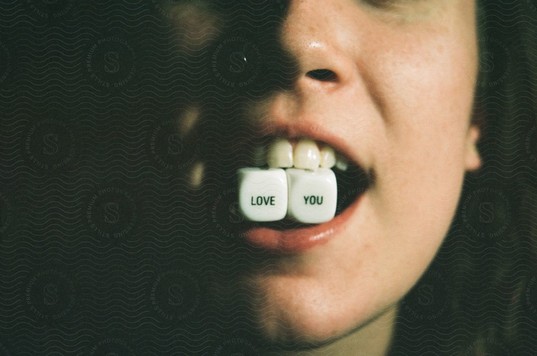 A person is holding two dice with their teeth that spells "love you".