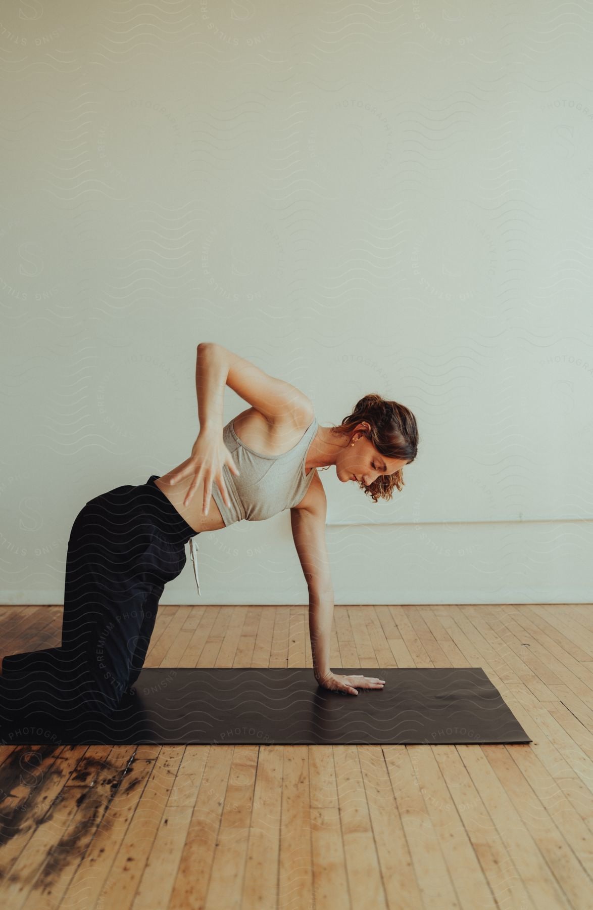 a young lady knee on a yoga mat, place her left hand straight on the mat and carry her right hand high up to her waistline