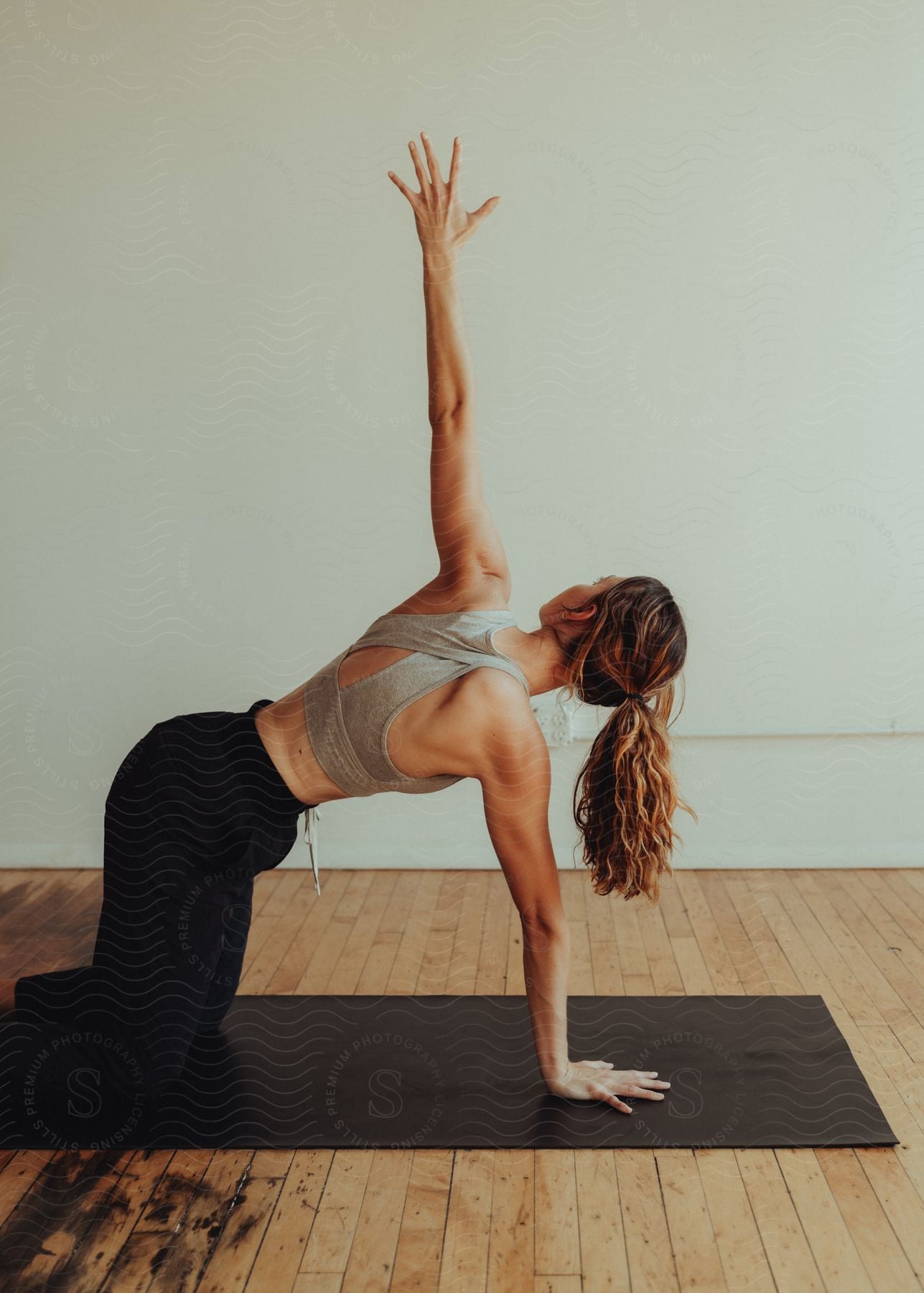 A woman kneels on an exercise mat resting on one arm with one hand stretched high in the air