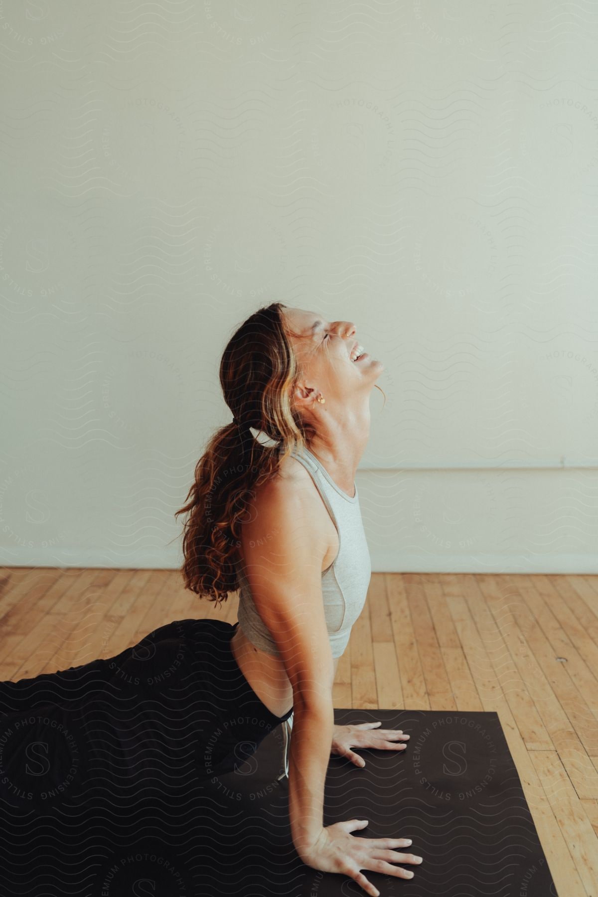 A woman smiles while she holds her upper torso upright as she performs a yoga pose.