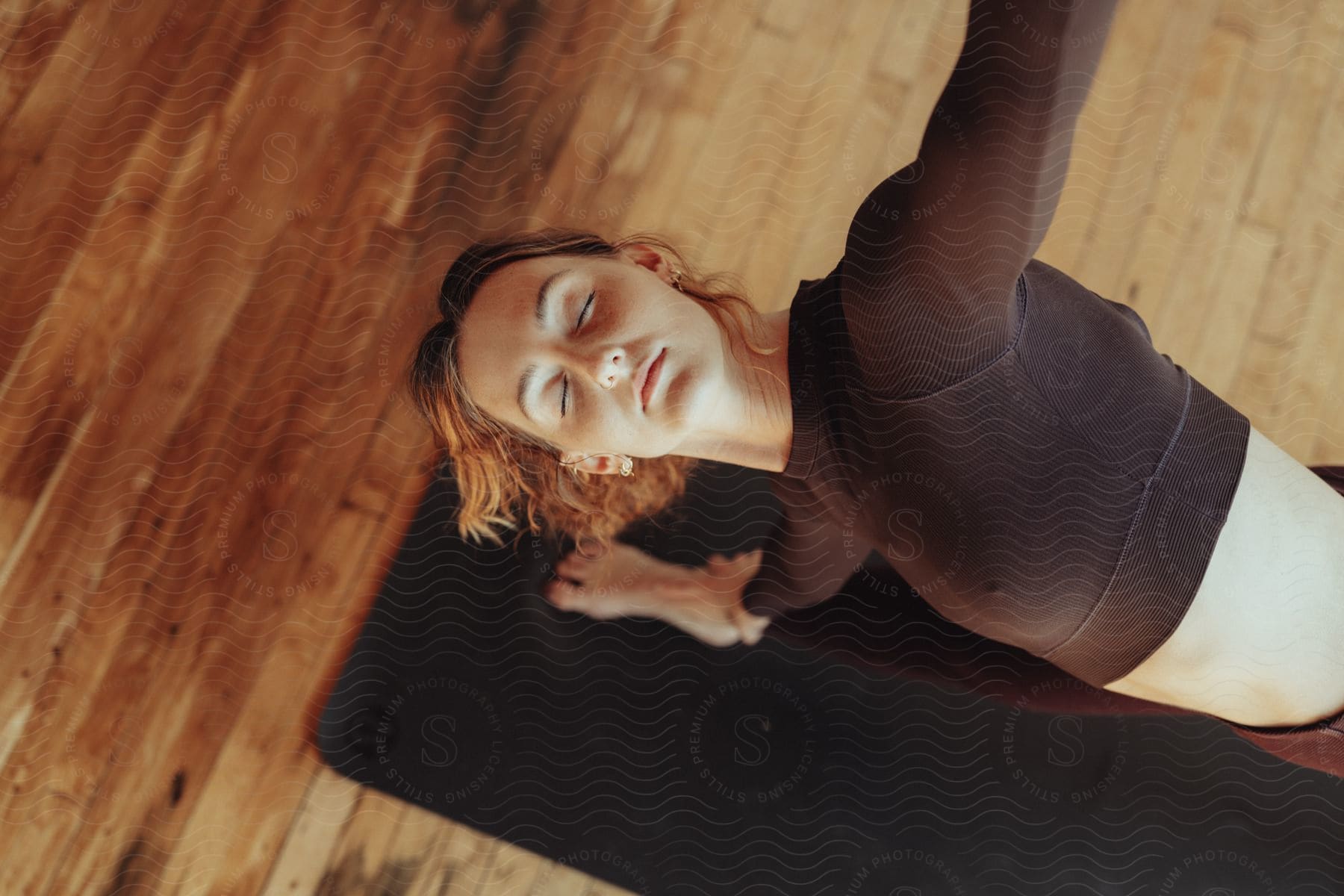 A woman in a meditative yoga pose on a black mat, her eyes closed and her face serene.