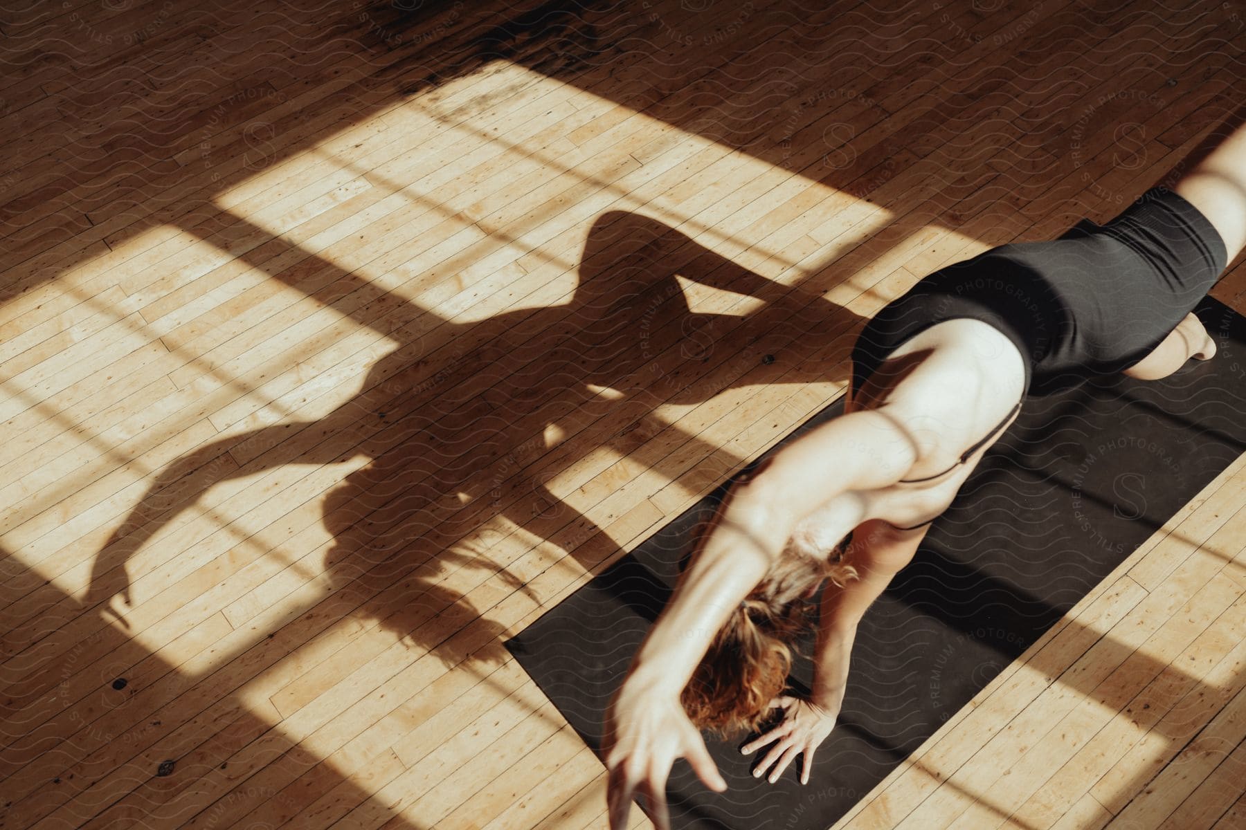 A woman is stretching on an exercise mat with an arm and a leg in the air as her shadow reflects on the floor