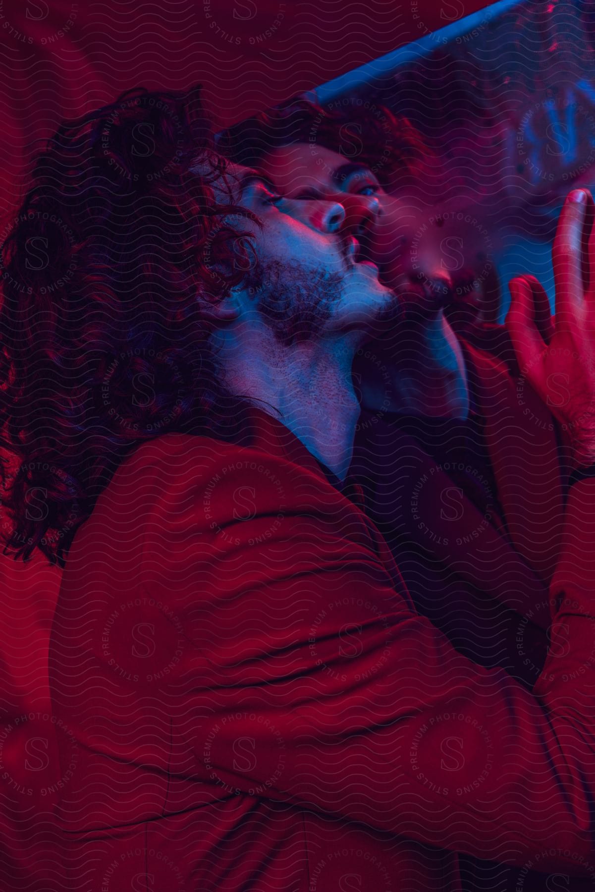 Man with wavy hair a beard and a red blazer jacket blows on a mirror