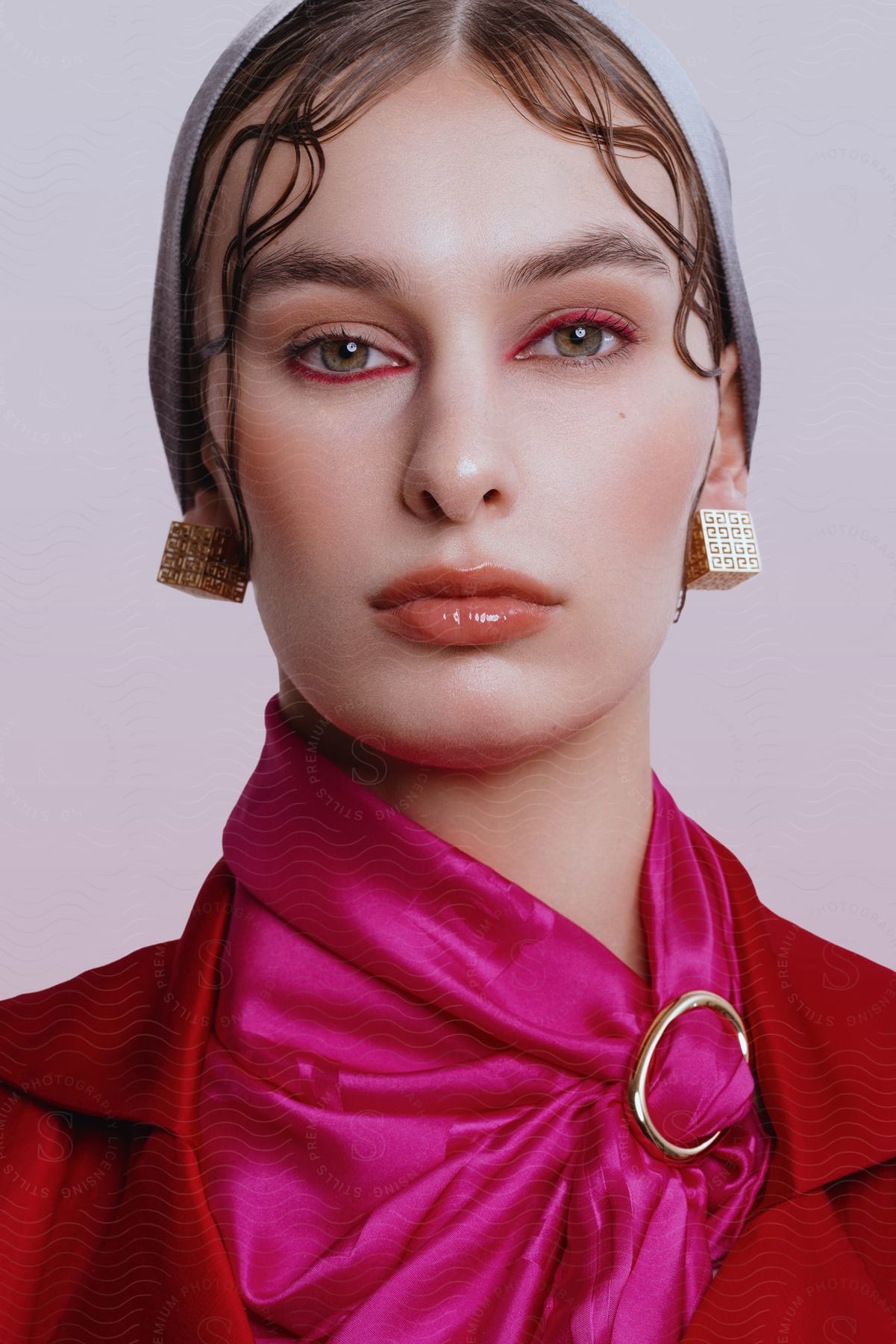 A woman posed with her mouth shut and eyes forward, wearing square earrings and red and pink clothing.