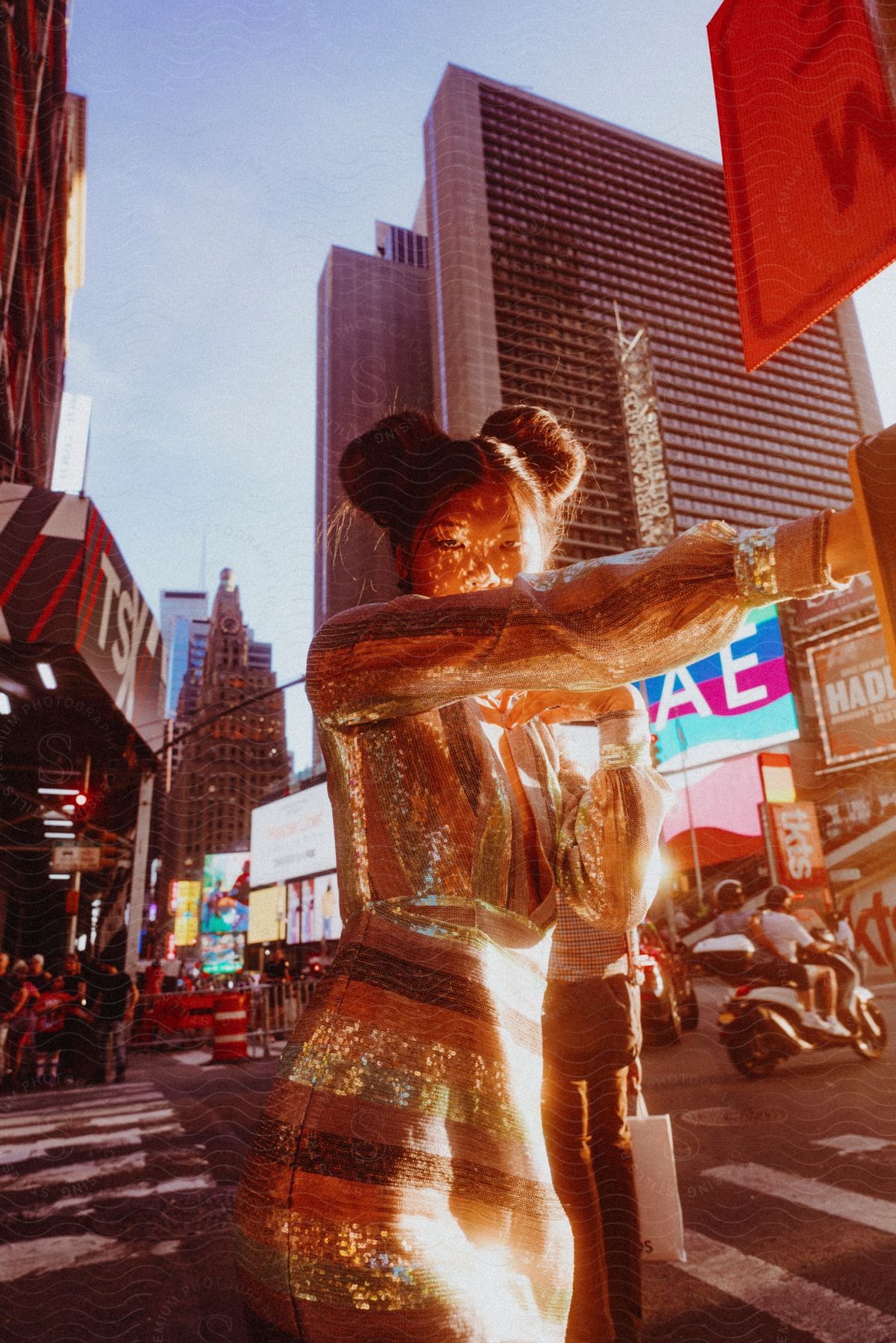 The sun shines brightly upon a woman standing on a downtown street with towers and buildings in the distance