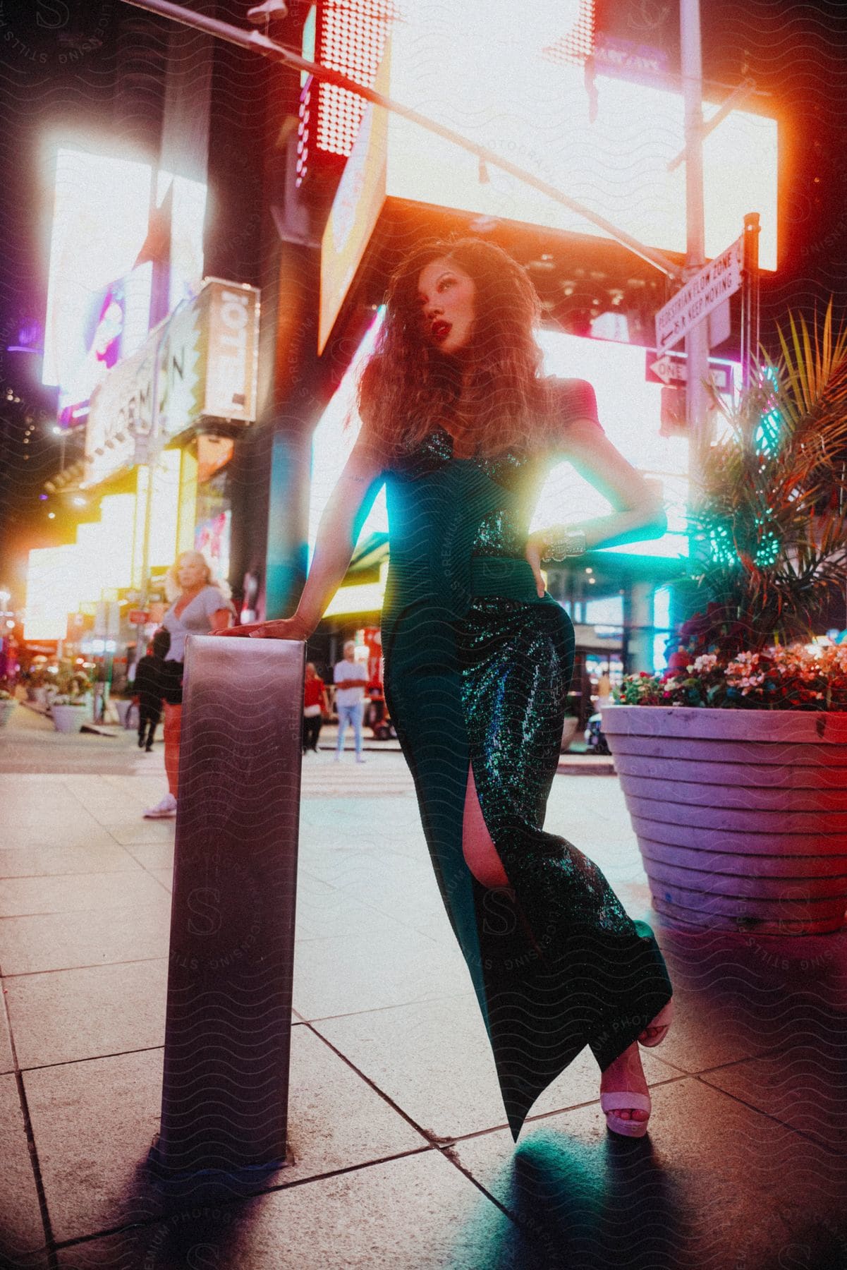 A women in a green sequenced dress is posing on the corner in a large city at night.