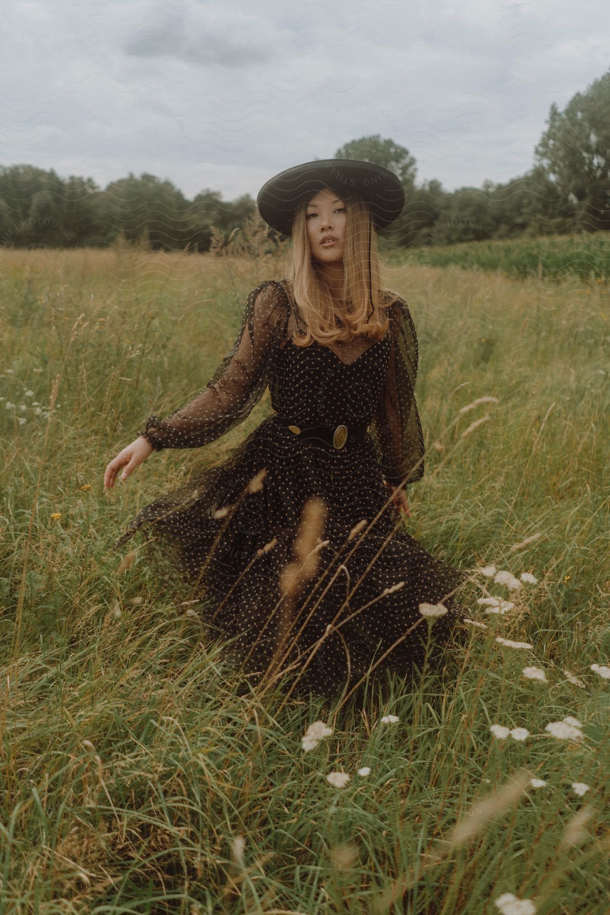 With a hat on her head, a lady in dress appears to be walking through a grassy field.