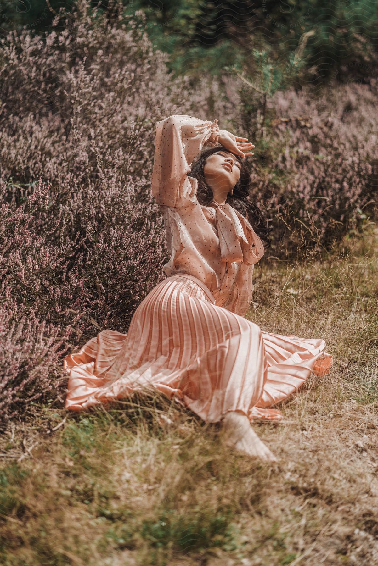 a woman leans back while lying on grass in a satin shirt and skirt