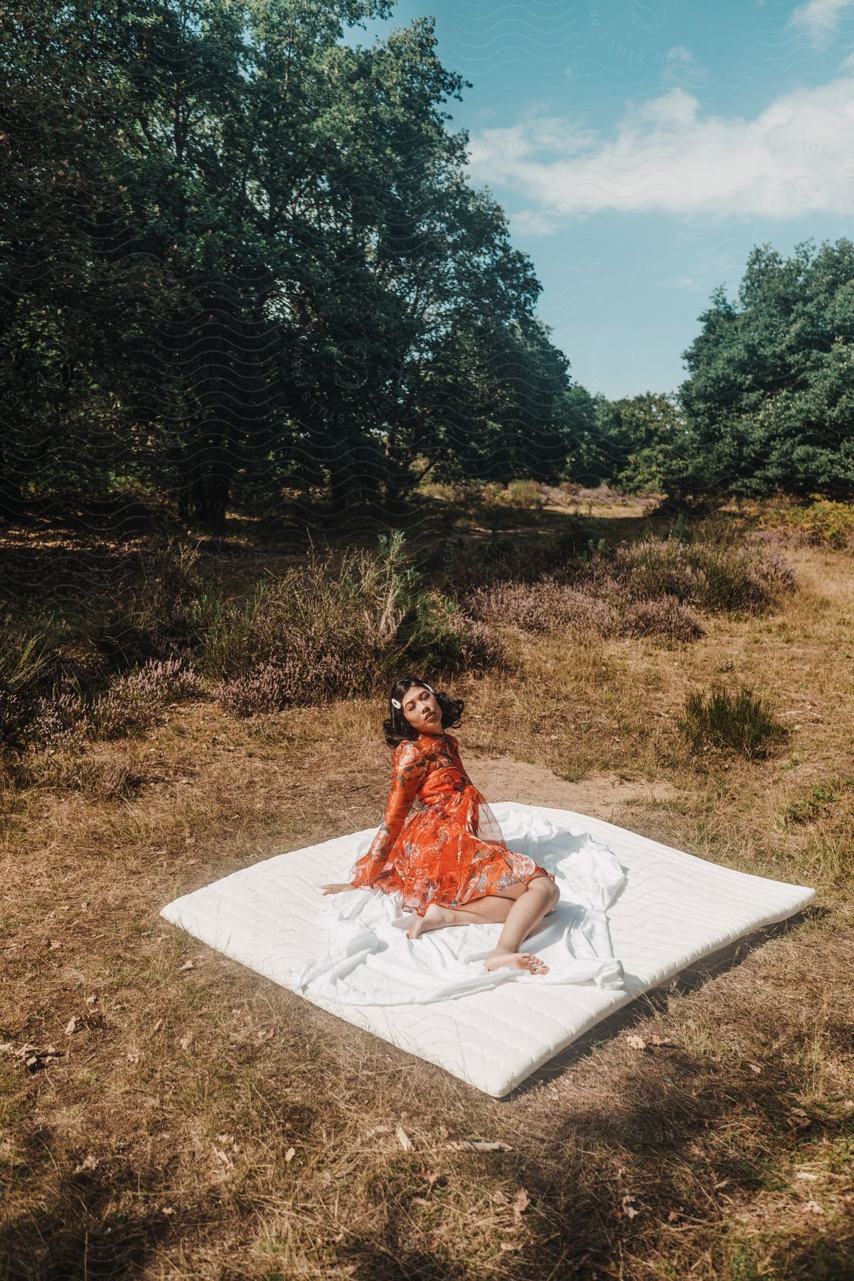 A young Asian woman models an orange dress while sitting on a mattress topper on the ground.