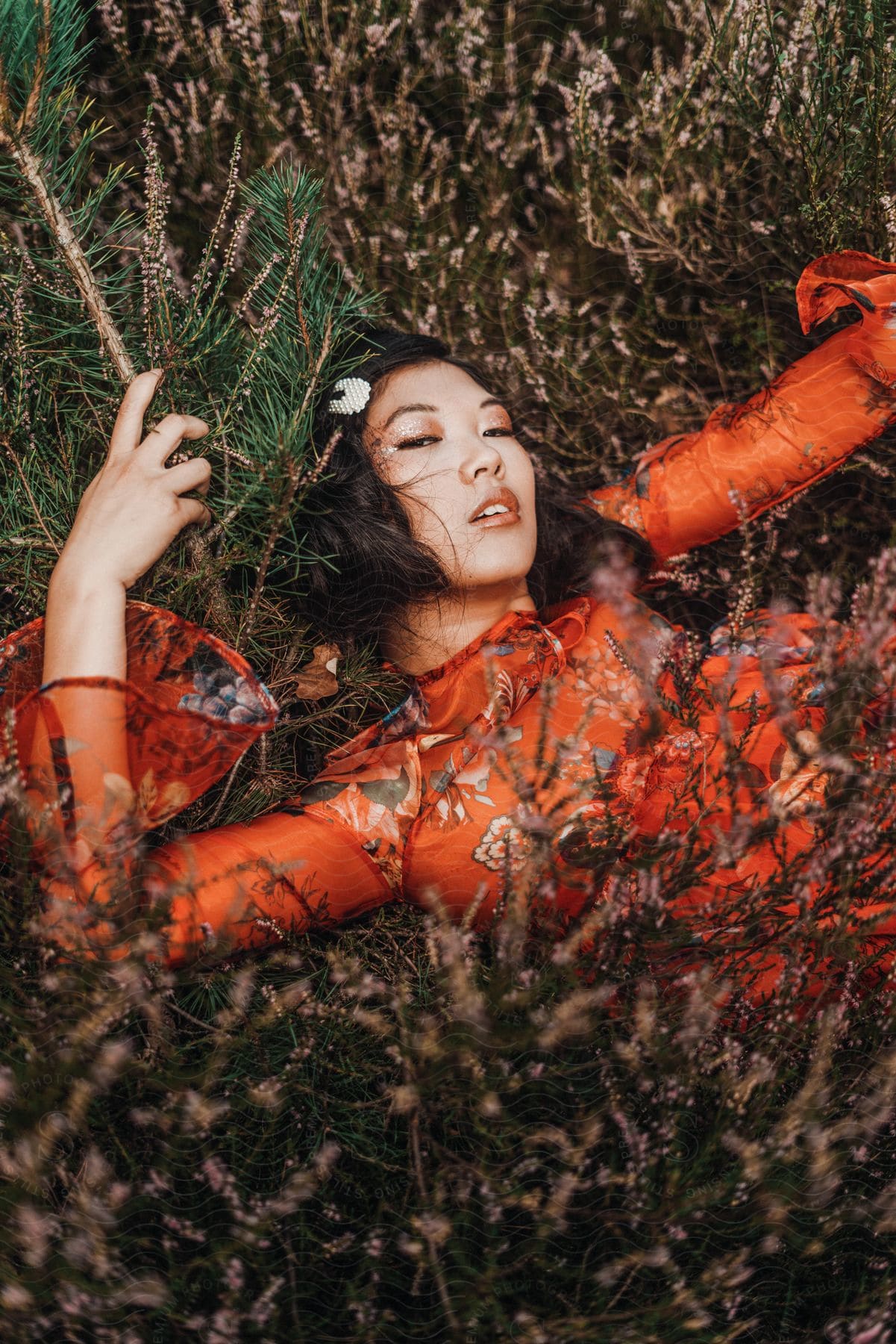 An asain women is laying in the tall wooded area in a red blouse.