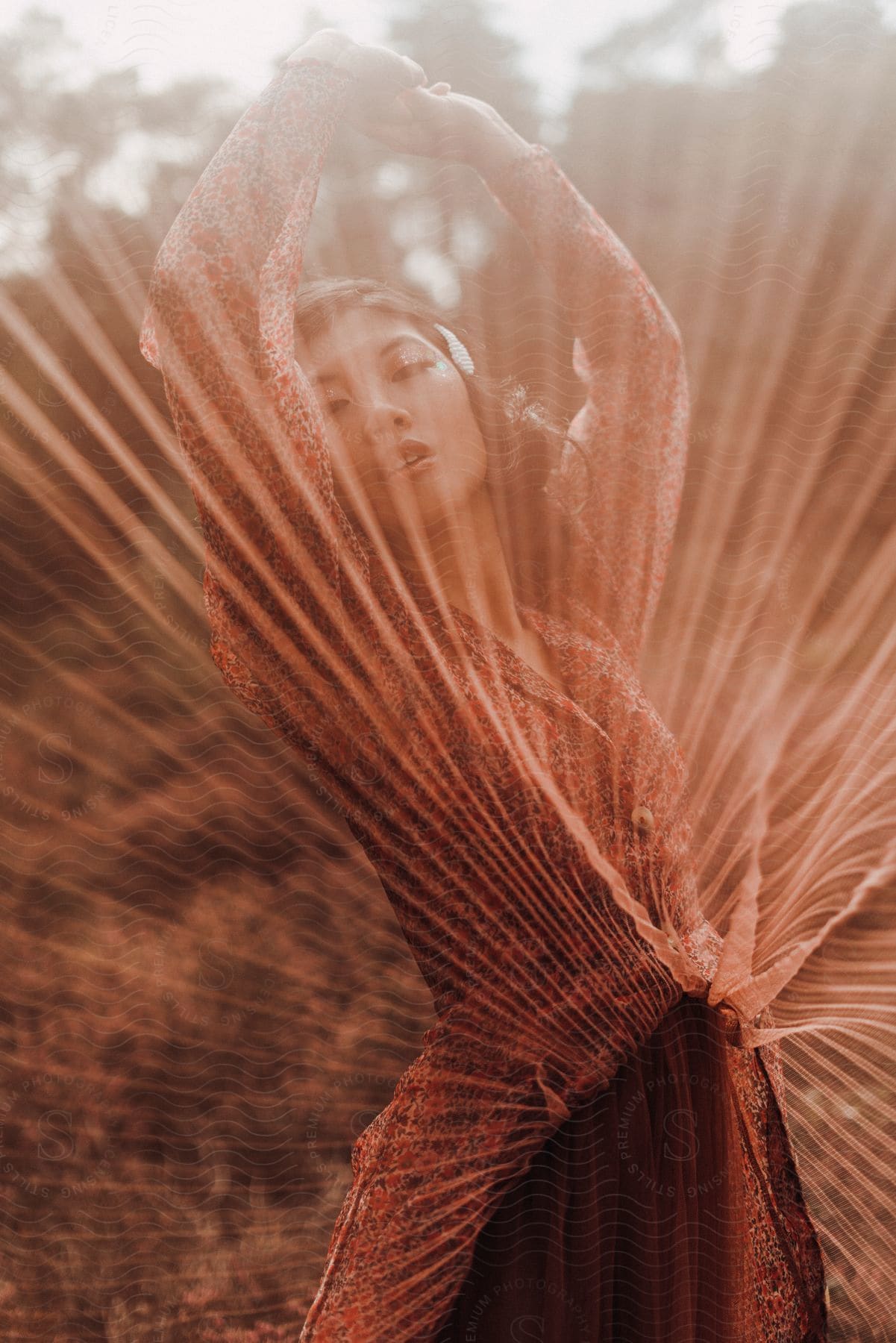 Woman lifts arms behind her red dress's skirt in a field.