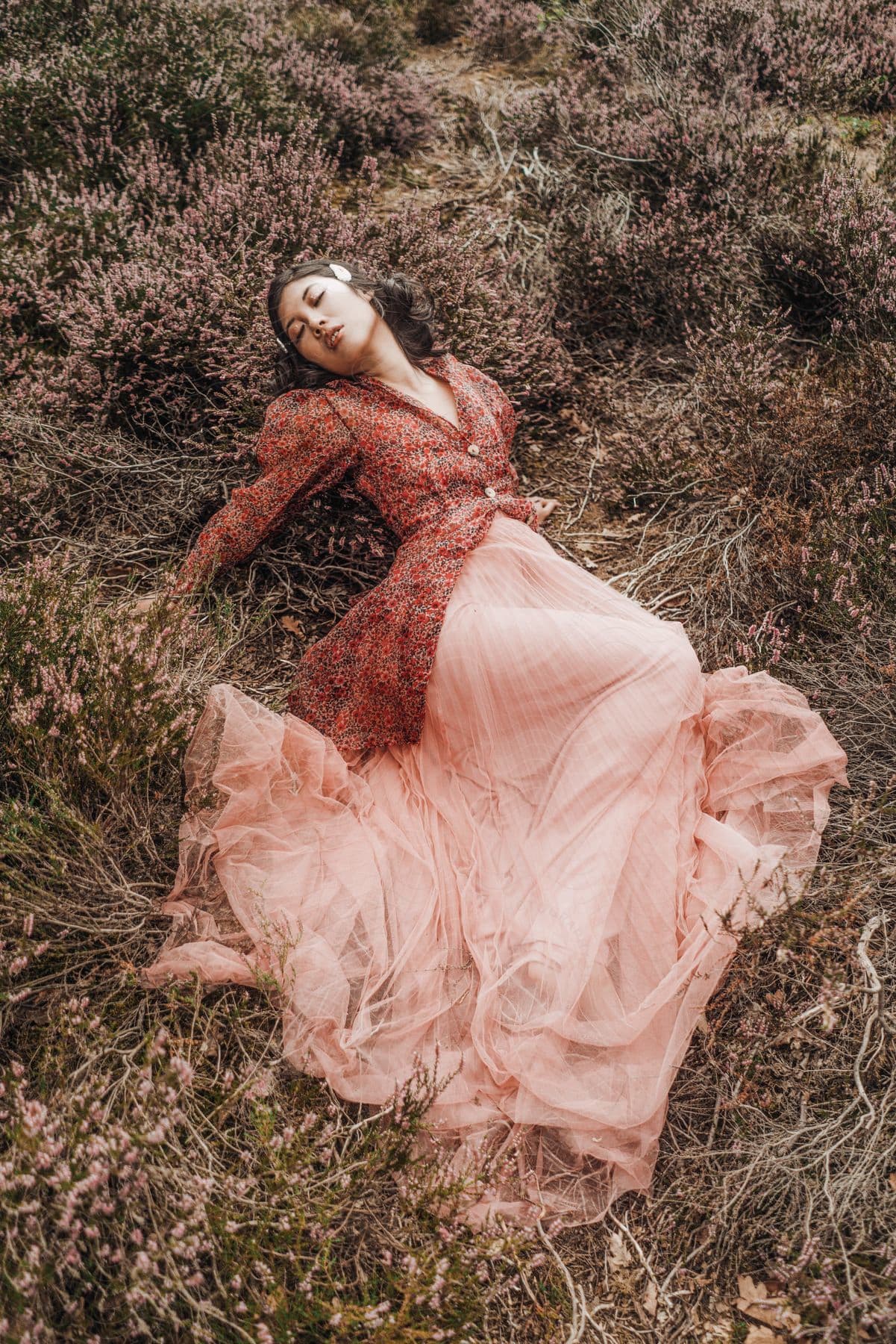 Female model lies among wildflowers in a pink skirt and a long blouse.