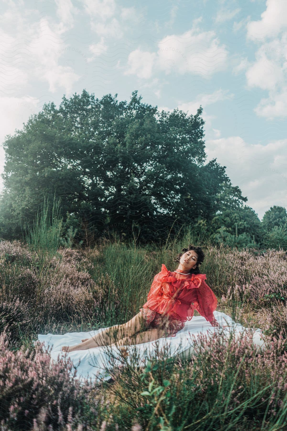 An Asian woman wears a ruffle outfit while posing on a towel in a grassy field.