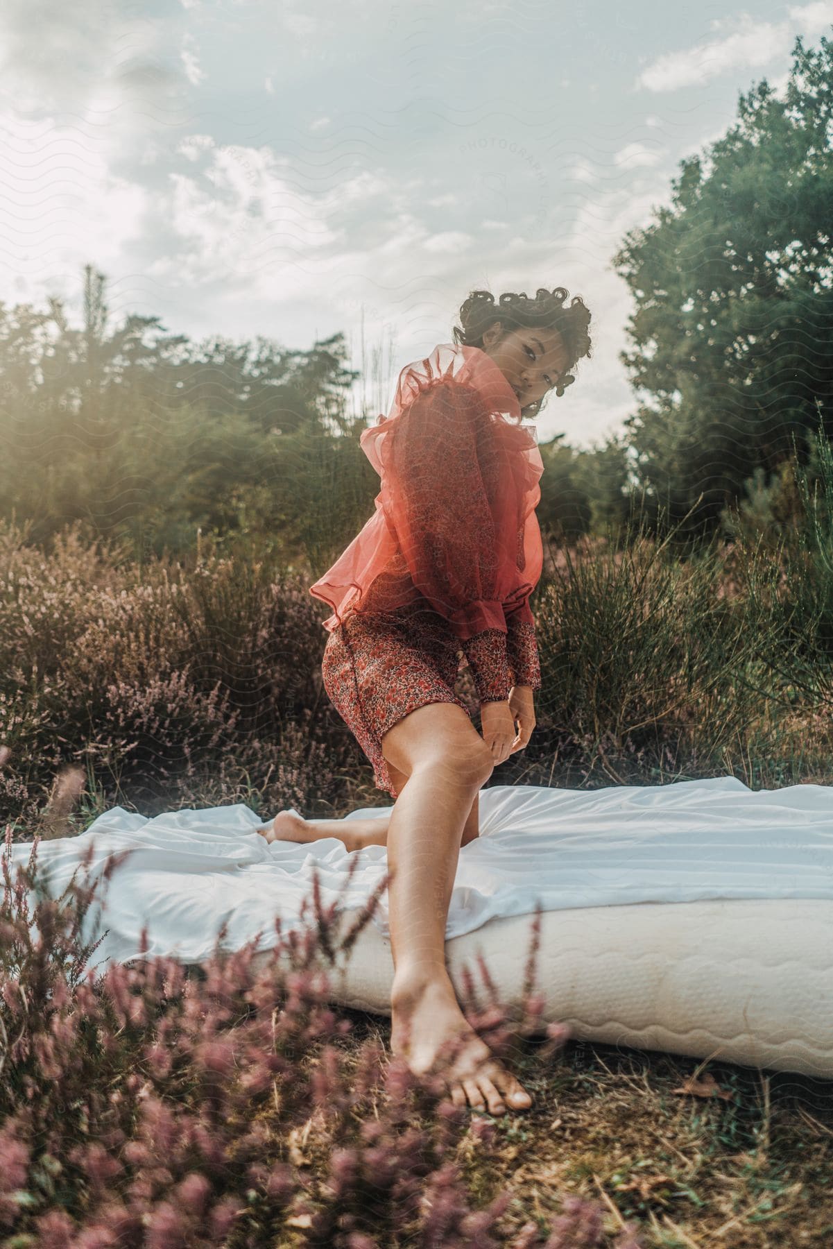 A woman modeling clothing in nature on a blow up mattress with  a white sheet on it.