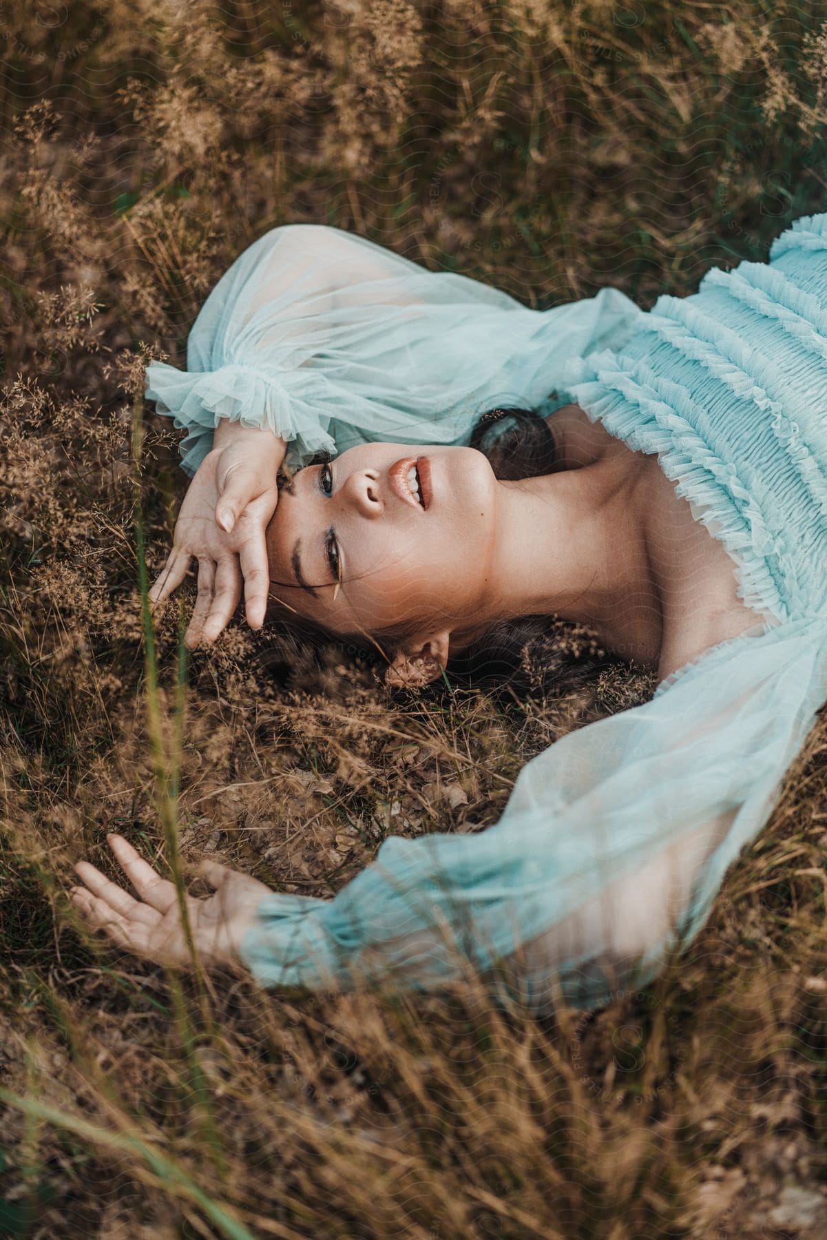 An Asian woman lays in a grassy field while wearing a dress with transparent sleeves.