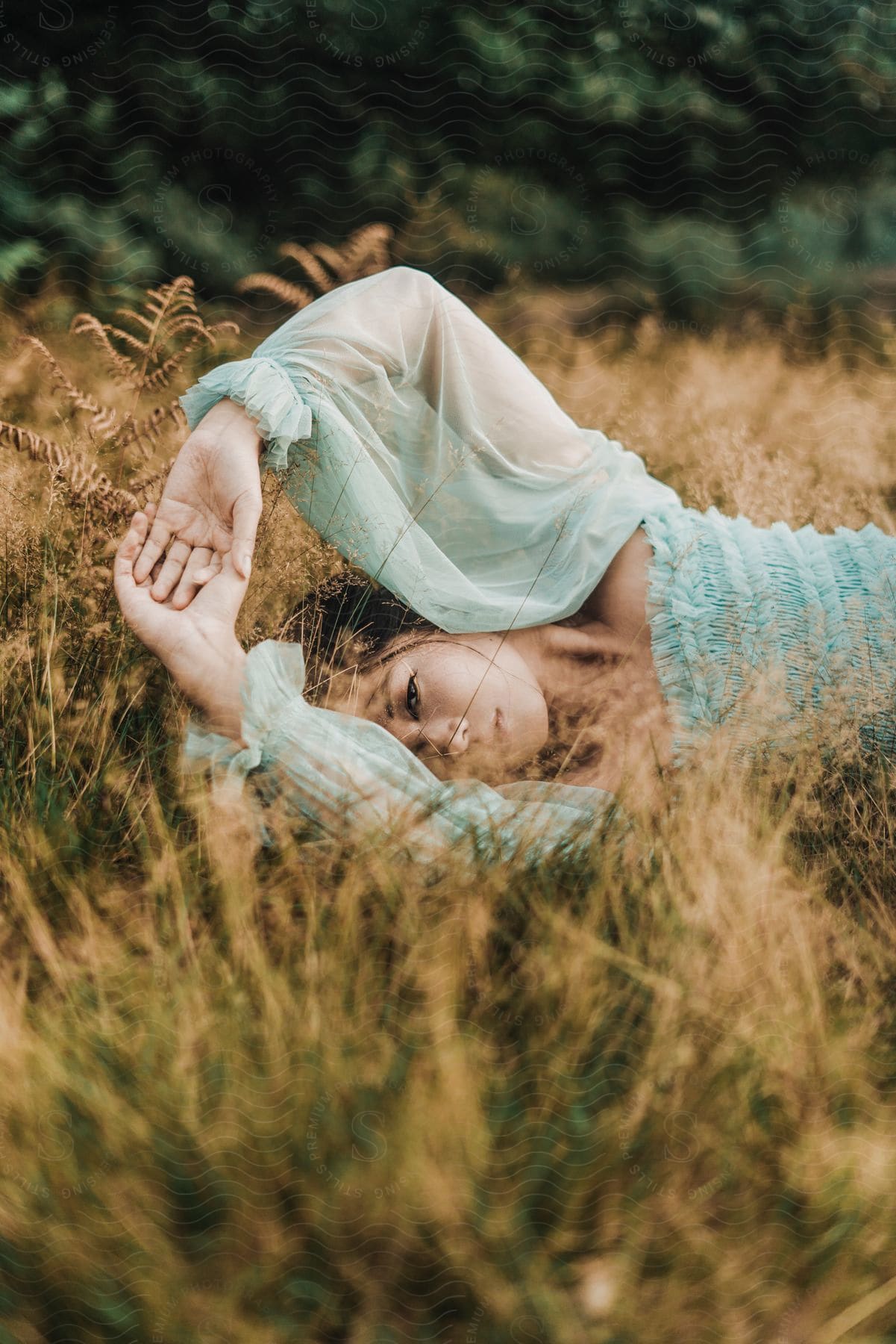 Stock photo of a young woman wears an aqua blue dress with long sleeves while lying in tall grass.